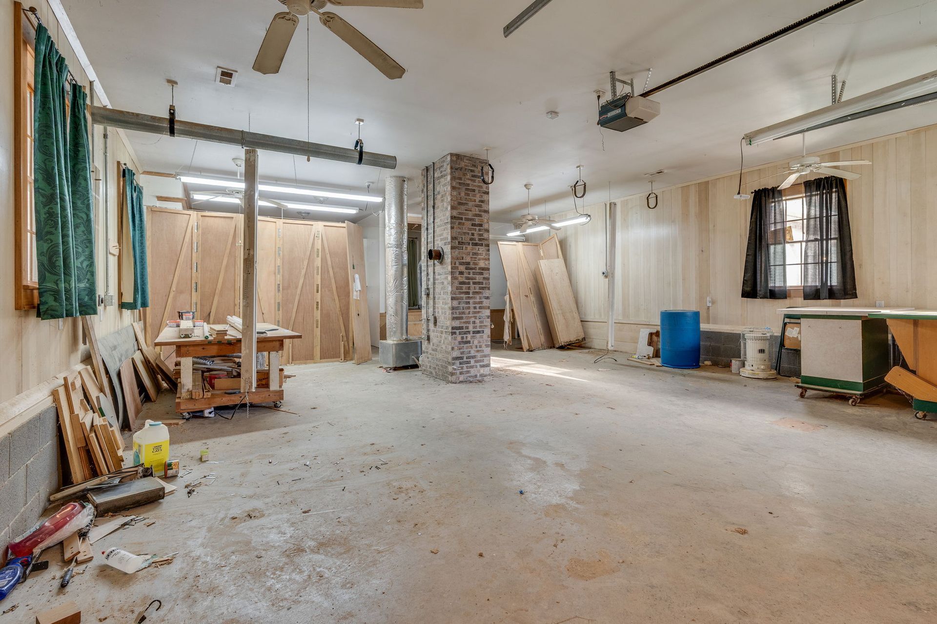 A cluttered workshop interior with a concrete floor, wooden panels, and a center brick column.