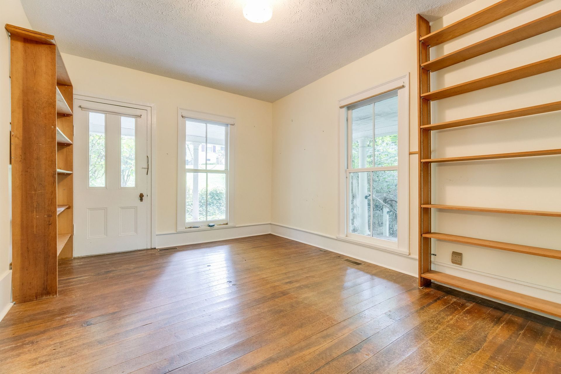 Empty unfurnished room with hardwood floors, built-in shelves, and two windows.
