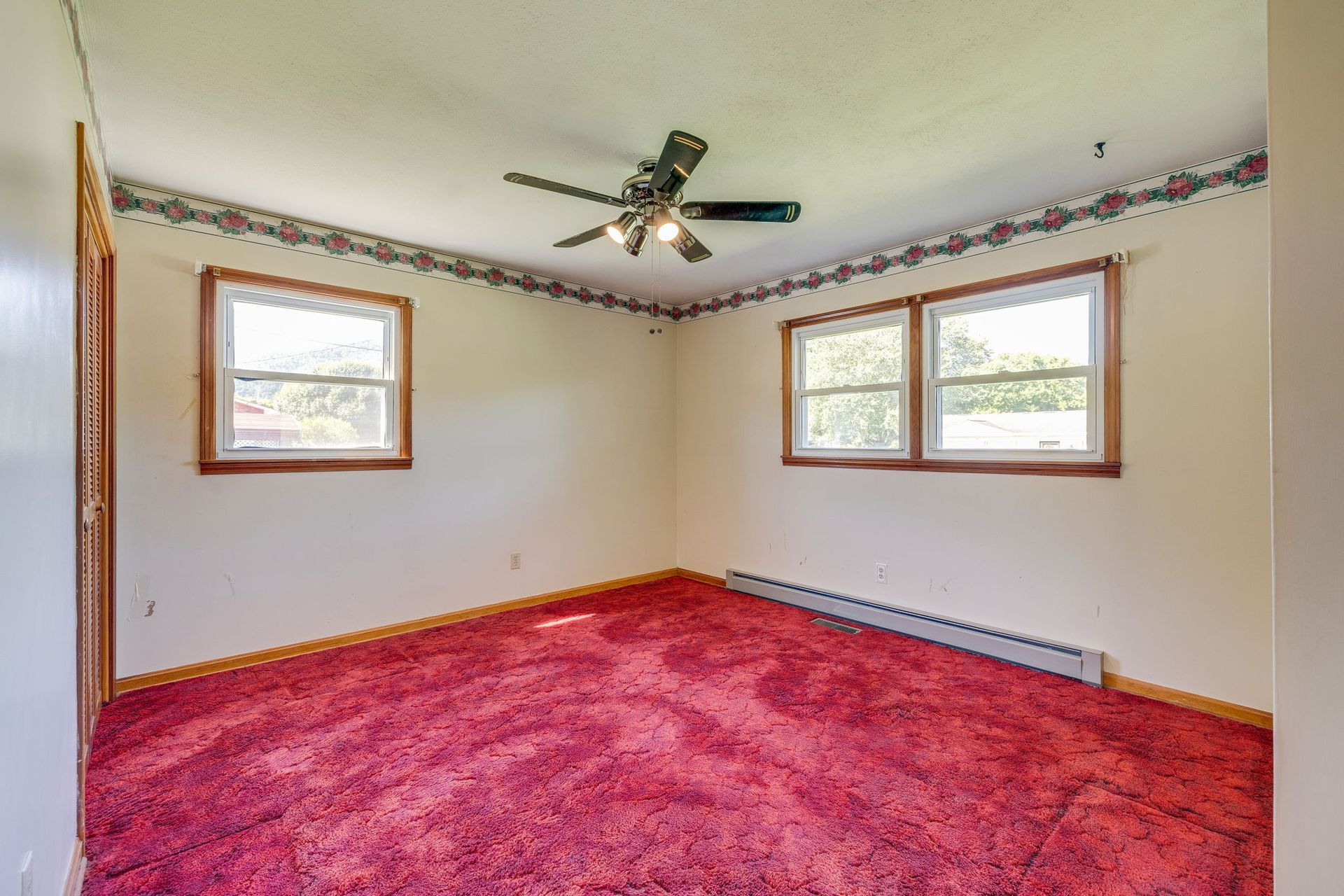 Empty bedroom with bright pink carpet, white walls, and three windows under a ceiling fan
