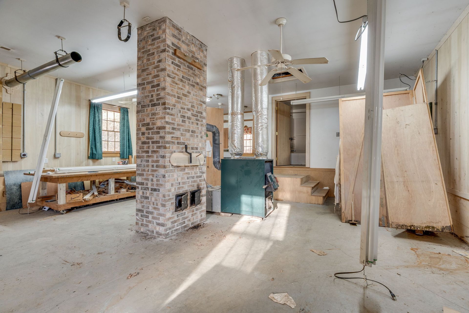 A spacious, unfinished room with a brick fireplace, a workbench, and exposed ductwork.