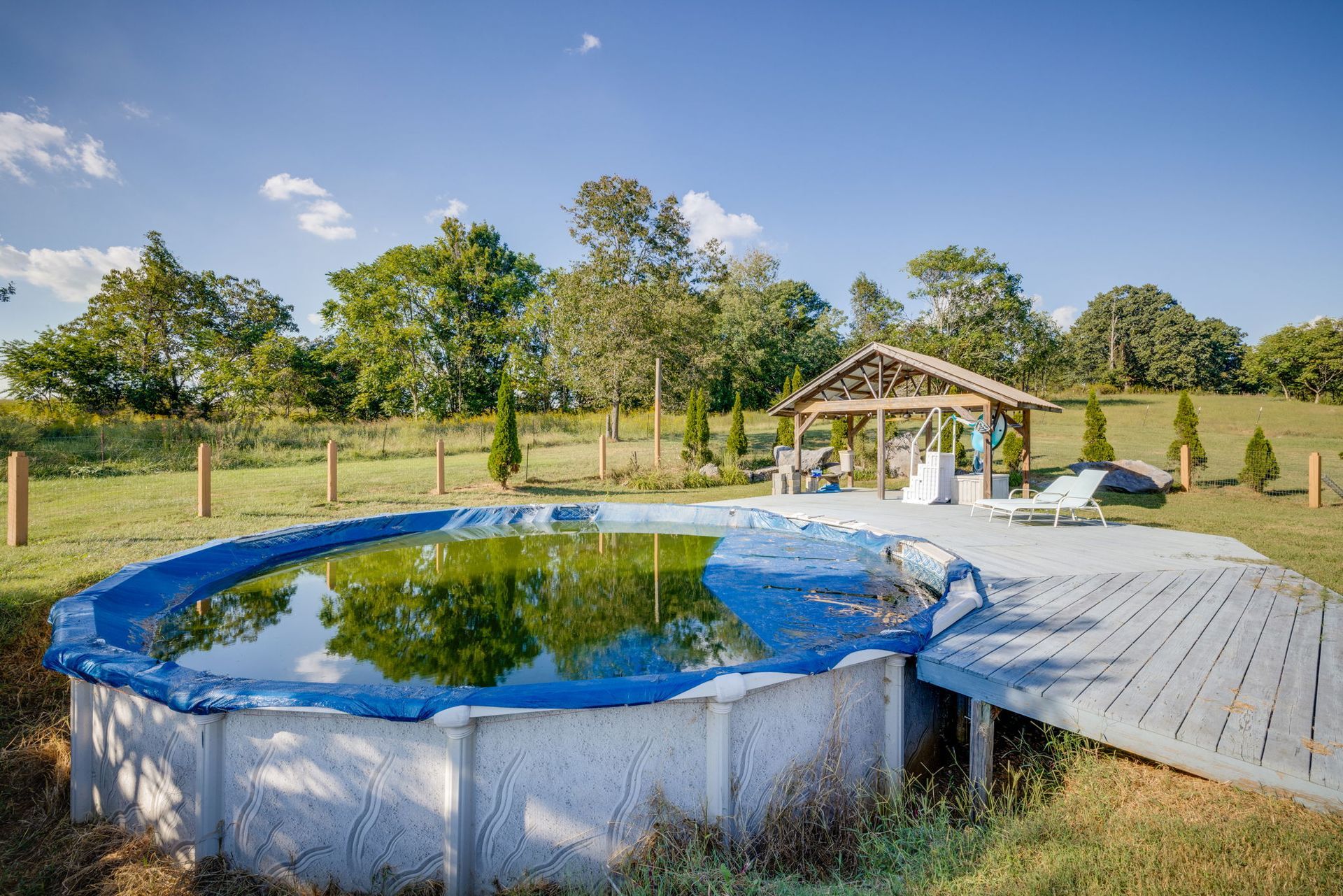 Backyard with above-ground pool, wooden deck, gazebo, and trees under a clear blue sky