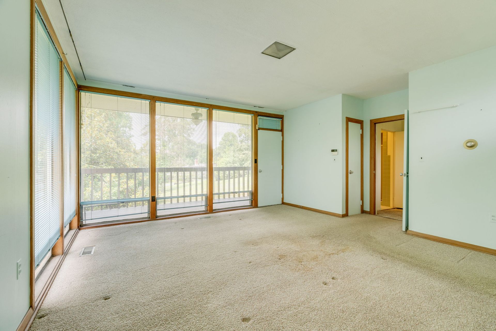 Empty carpeted living room with large windows and sliding glass door, light green walls, and balcony view