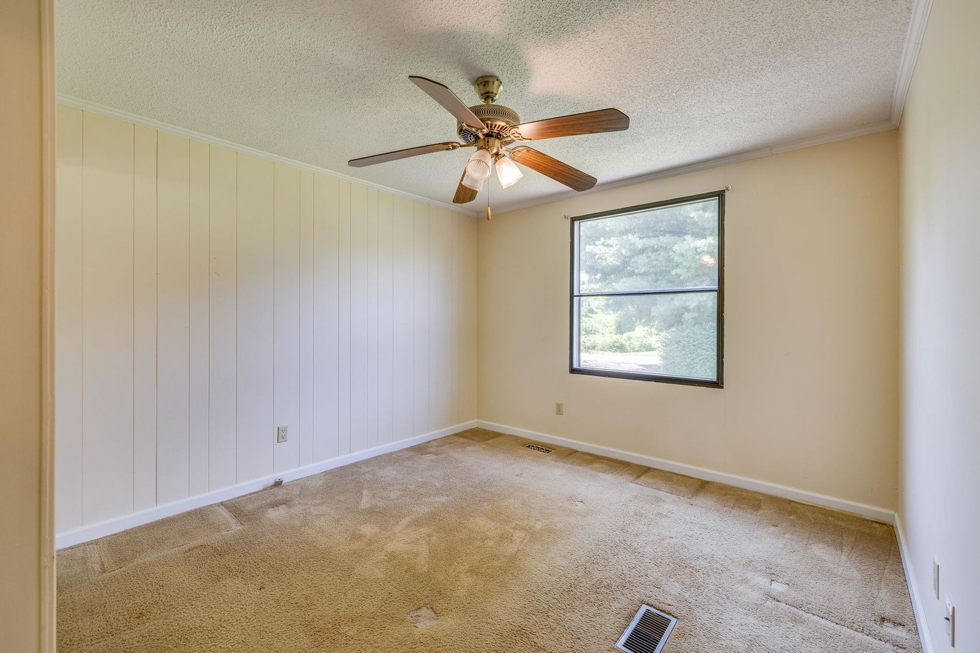 Empty beige bedroom with carpet, white closet doors, ceiling fan, and a window.