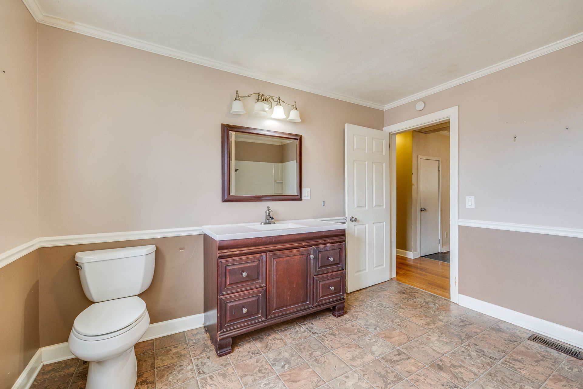 Bathroom with white toilet, dark wood vanity, mirror, and beige walls with white trim.
