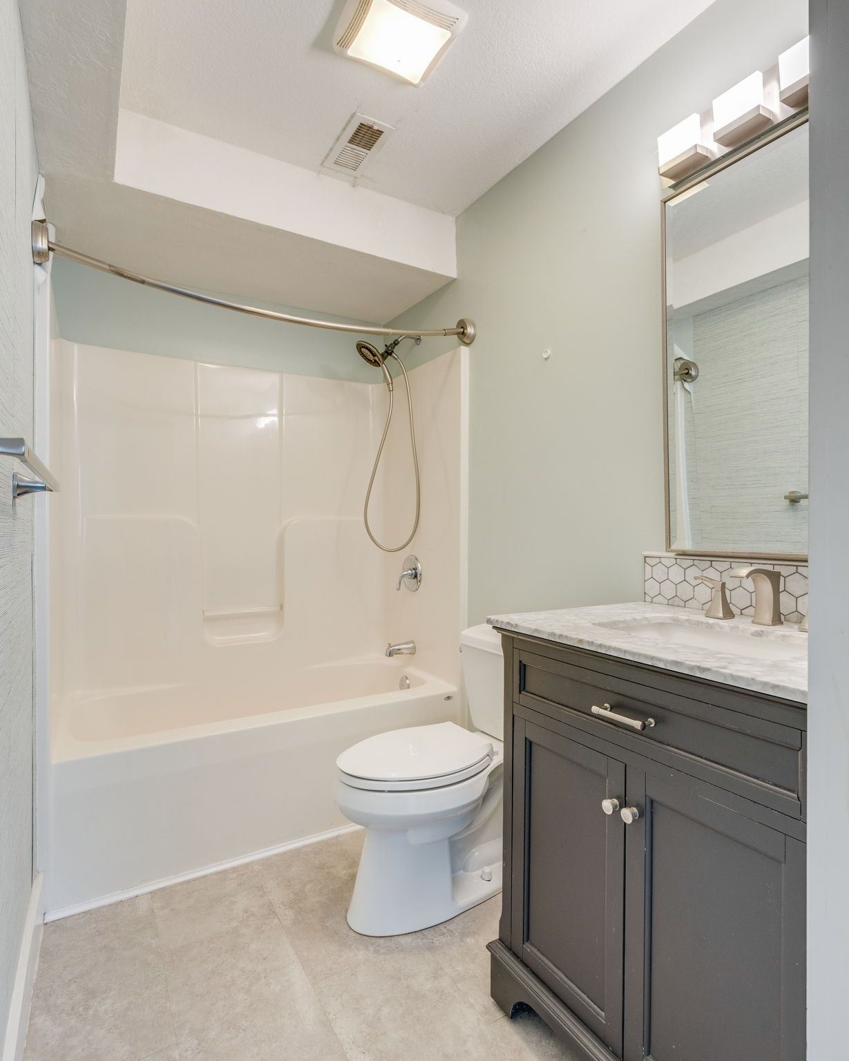 Small bathroom with white tub, toilet, and dark vanity with marble countertop and mirror.
