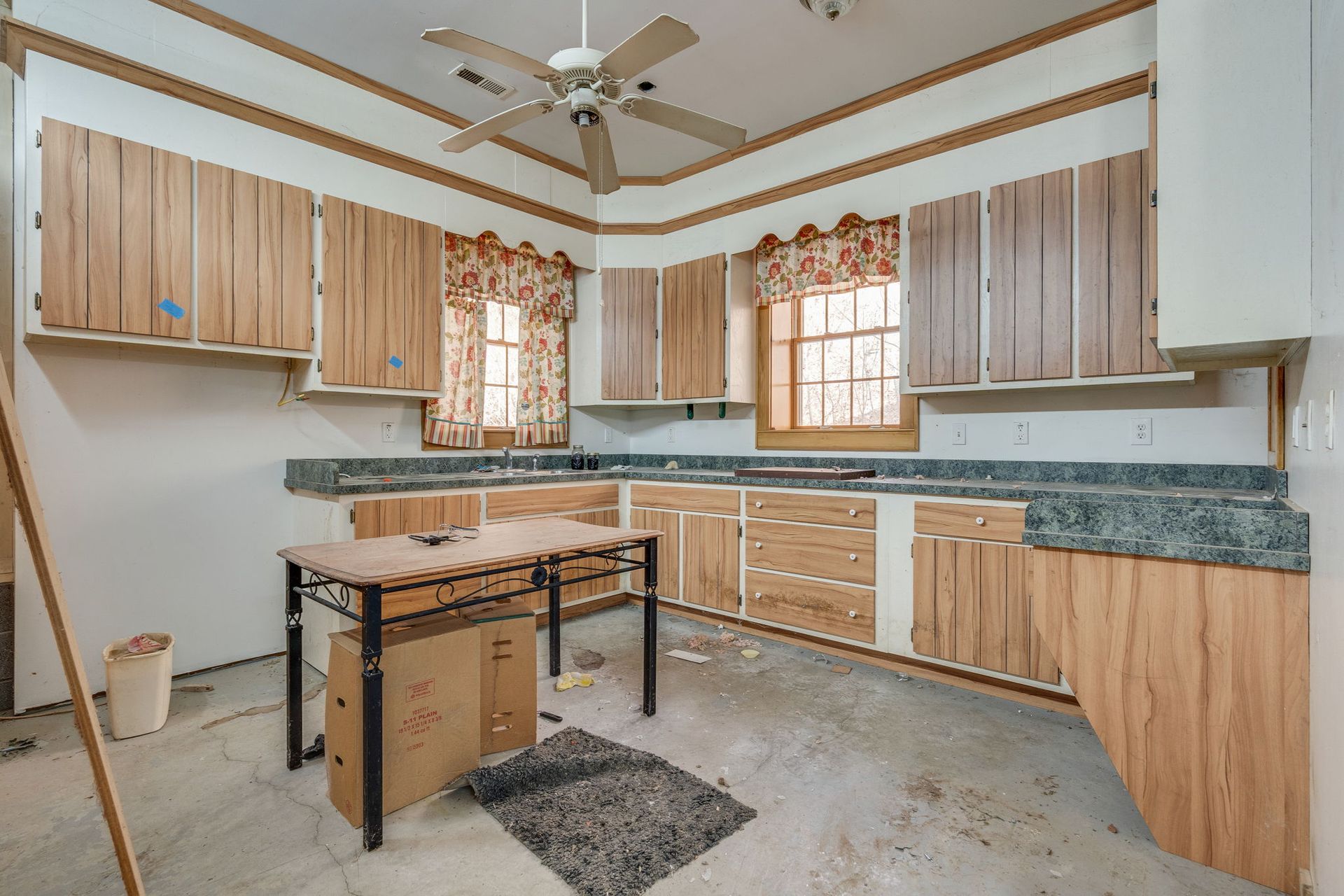 A kitchen with light wood cabinets and gray countertops. A small table sits in the center.