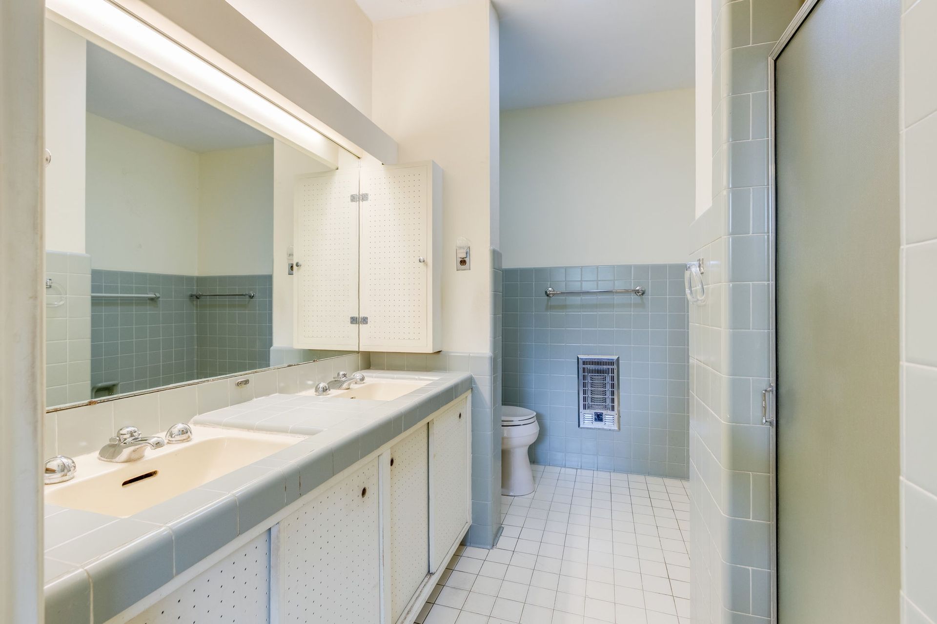 Bright bathroom with double sink vanity, large mirror, blue tile accents, and a shower stall.