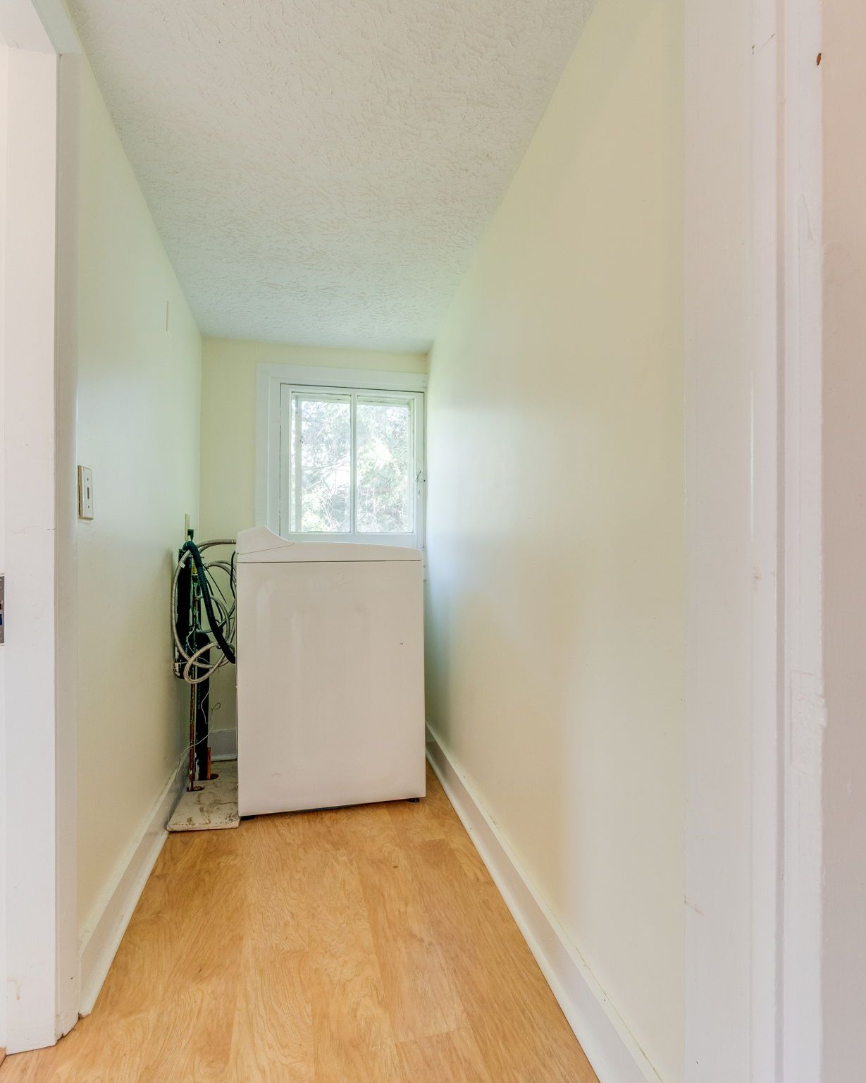 Narrow hallway with light wood floor, white walls, and a small cabinet beneath a window at the end.