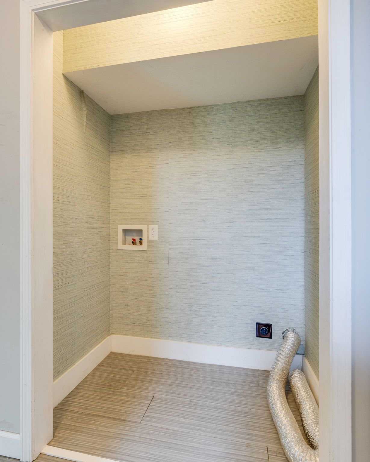 Empty recessed nook with wallpaper, outlet panel, and coiled hose on the floor