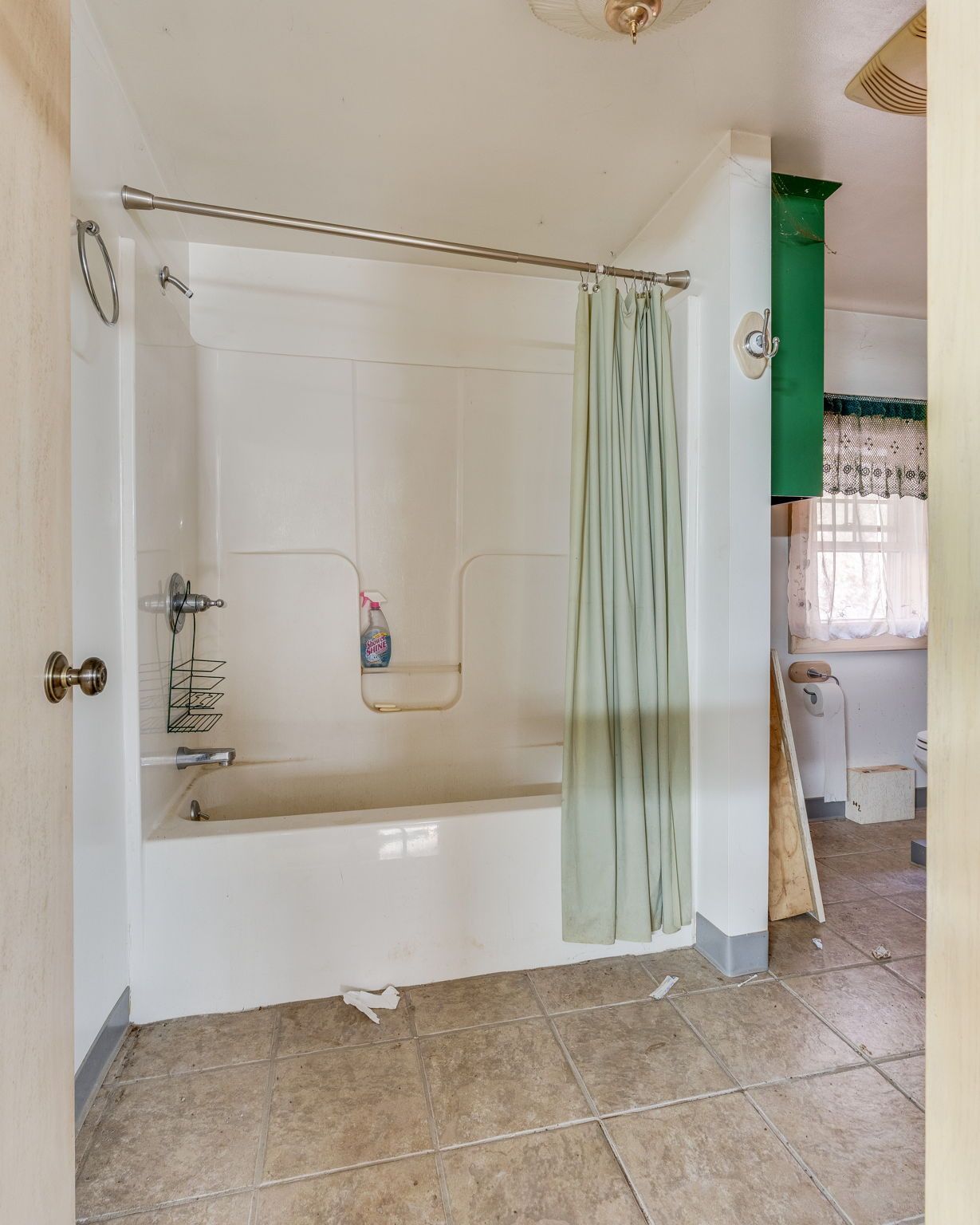 Bathroom with a white bathtub and shower curtain, green cabinet. Tiled floor.
