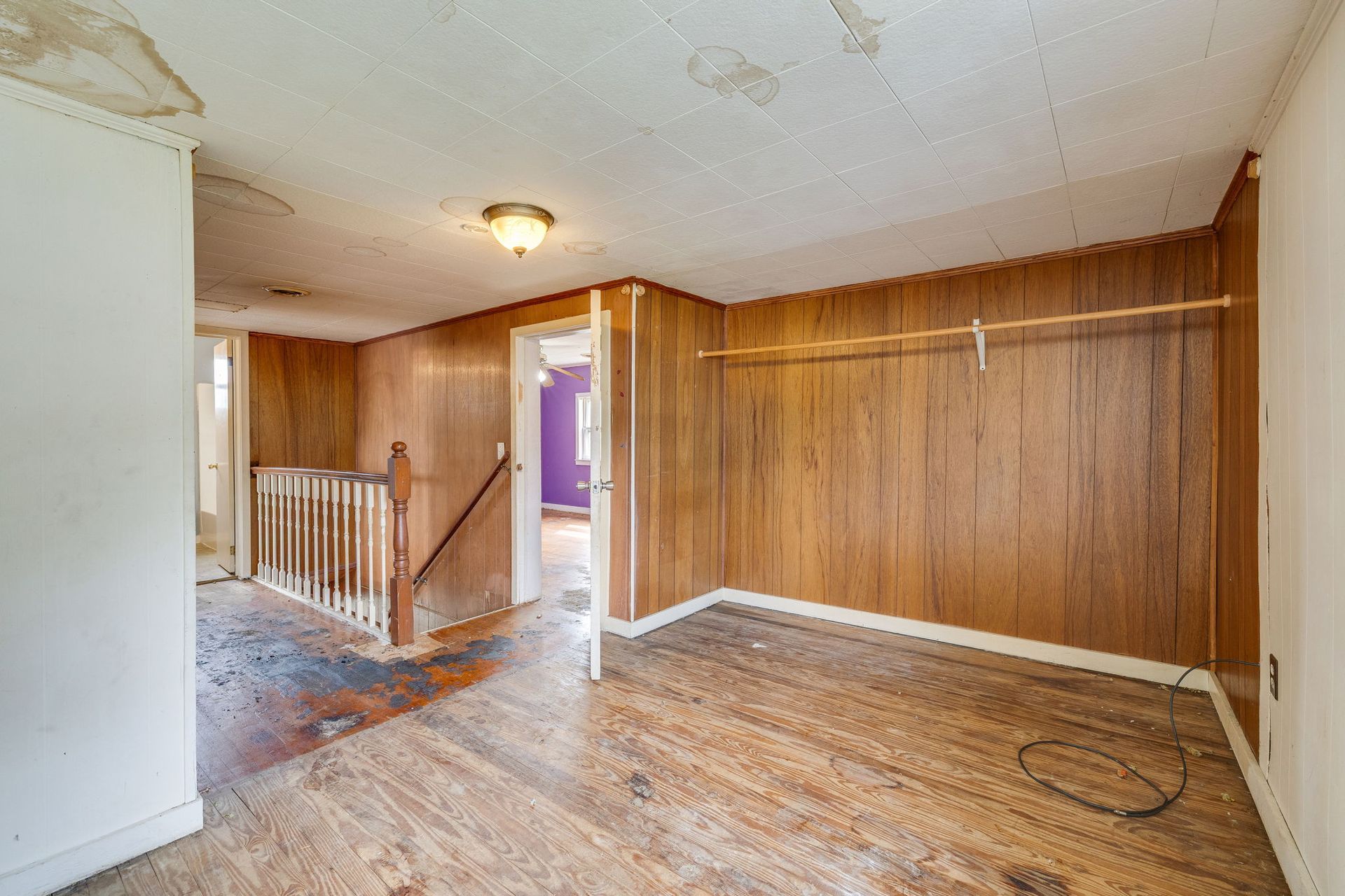 Empty wood-paneled room with worn carpet, staircase, and open doorway with purple light