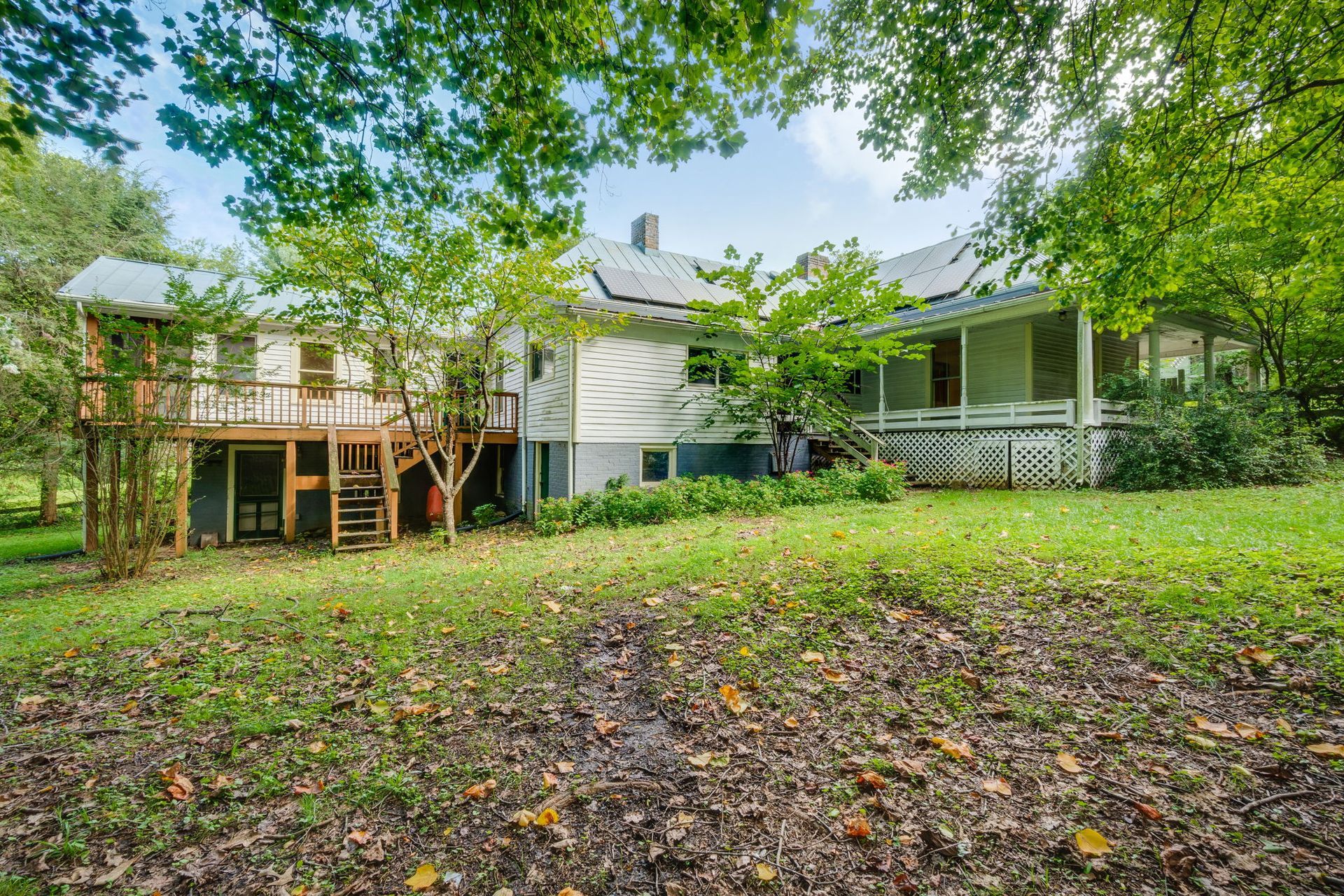 Leafy backyard with raised deck on the left, covered porch on the right, and a white house under green trees