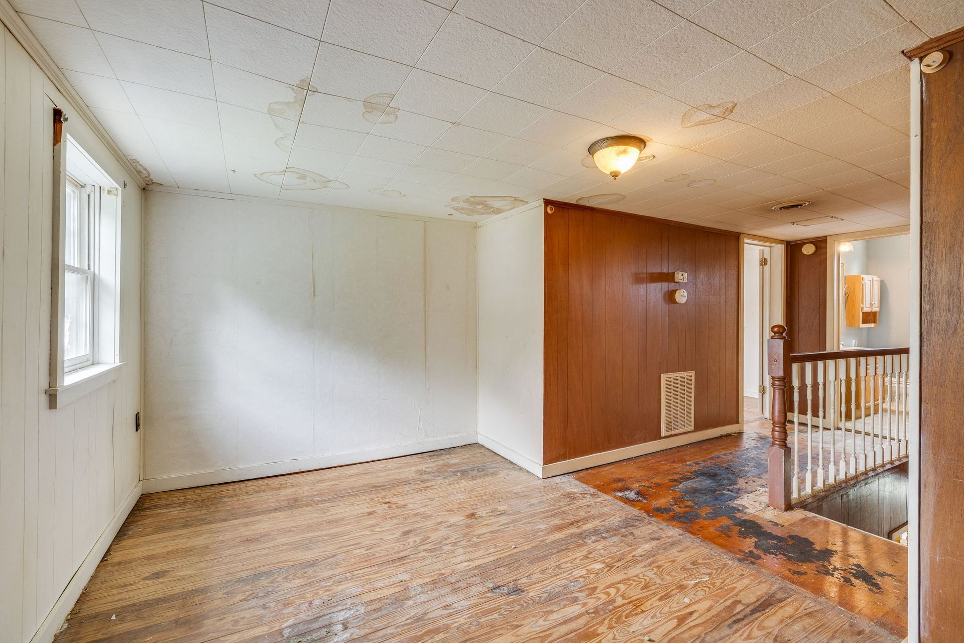 Empty living room with wood floor, white walls, and a brown accent wall by a stair railing
