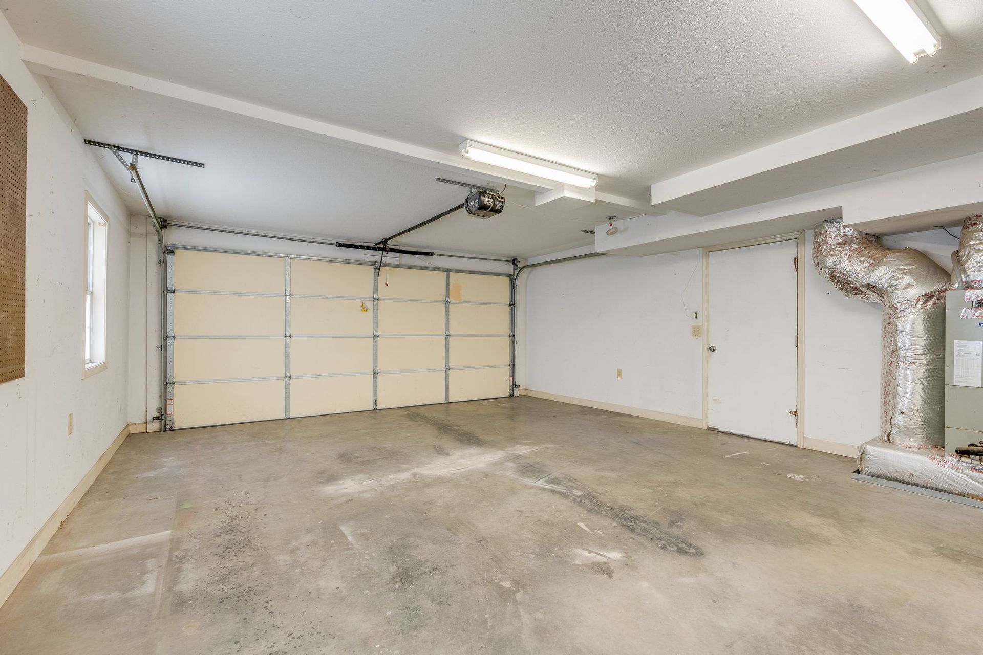 Empty garage with concrete floor, white walls, overhead lights, and a closed beige garage door.