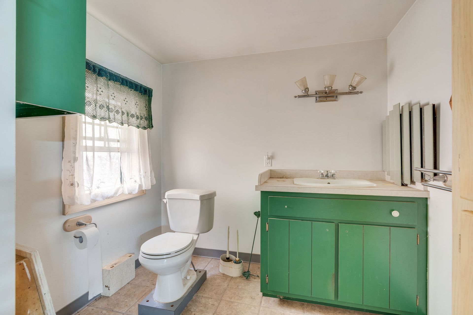 Bathroom with green vanity and cabinets, toilet, and radiator. Window has floral valance and white curtains.