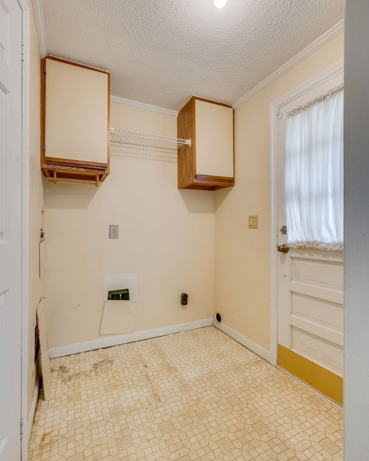 Small laundry room with wall cabinets, beige walls, and a windowed back door.