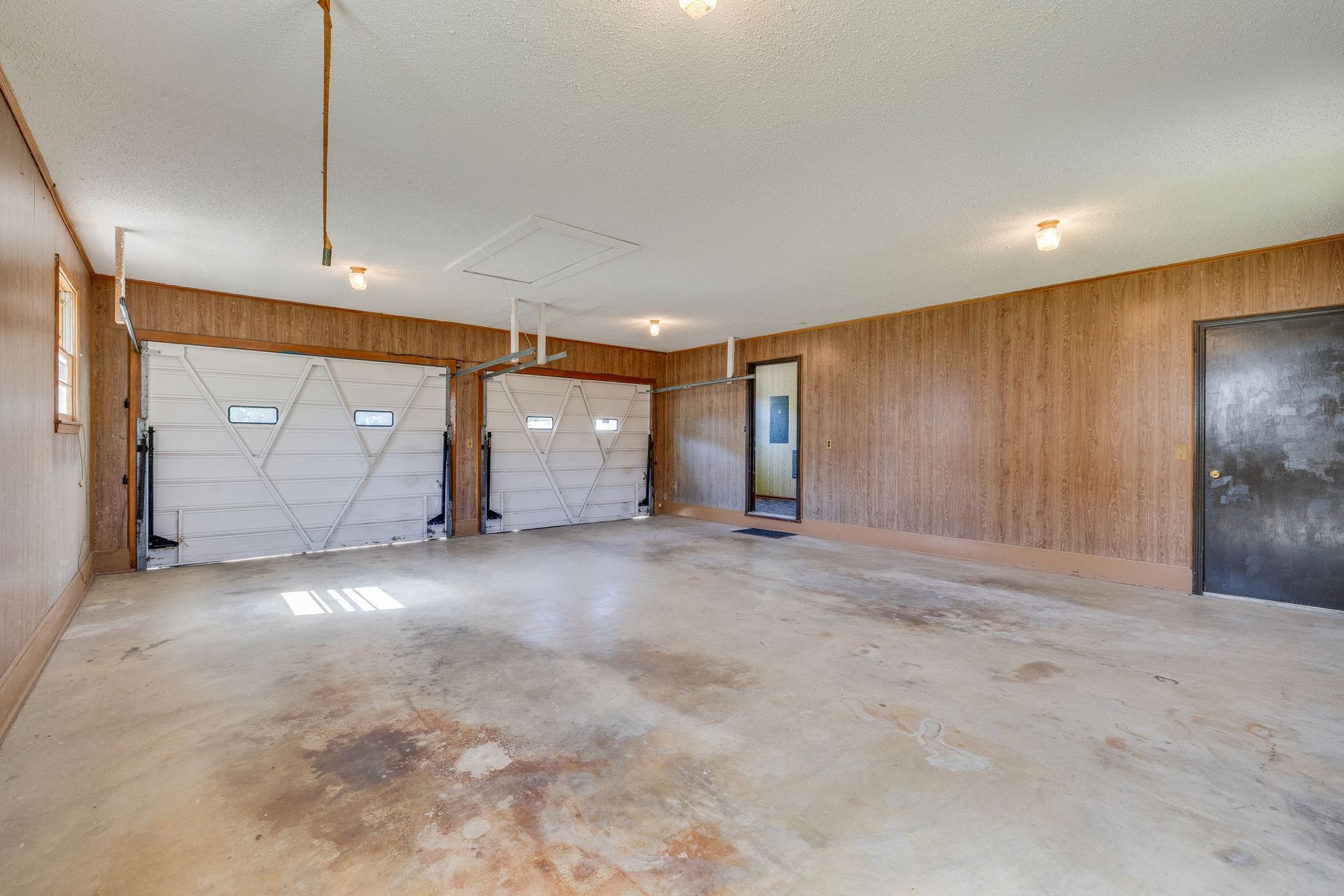 Empty two-car garage with wood-paneled walls, concrete floor, and garage doors on the left.