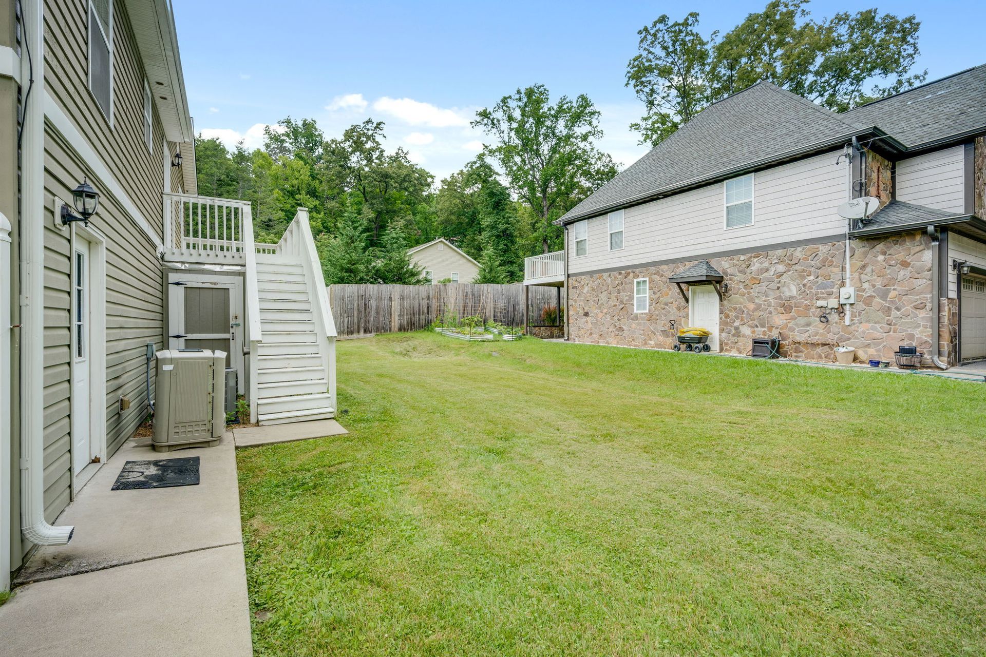 Backyard with green lawn, concrete patio, and two houses beside a wooden fence.