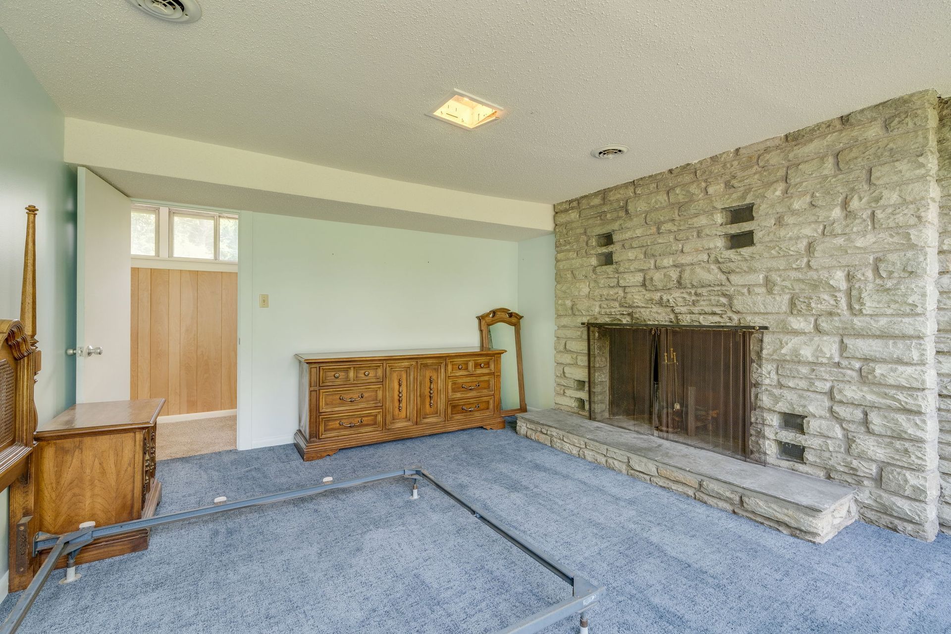 Empty living room with blue carpet, wooden cabinets, and a stone fireplace wall