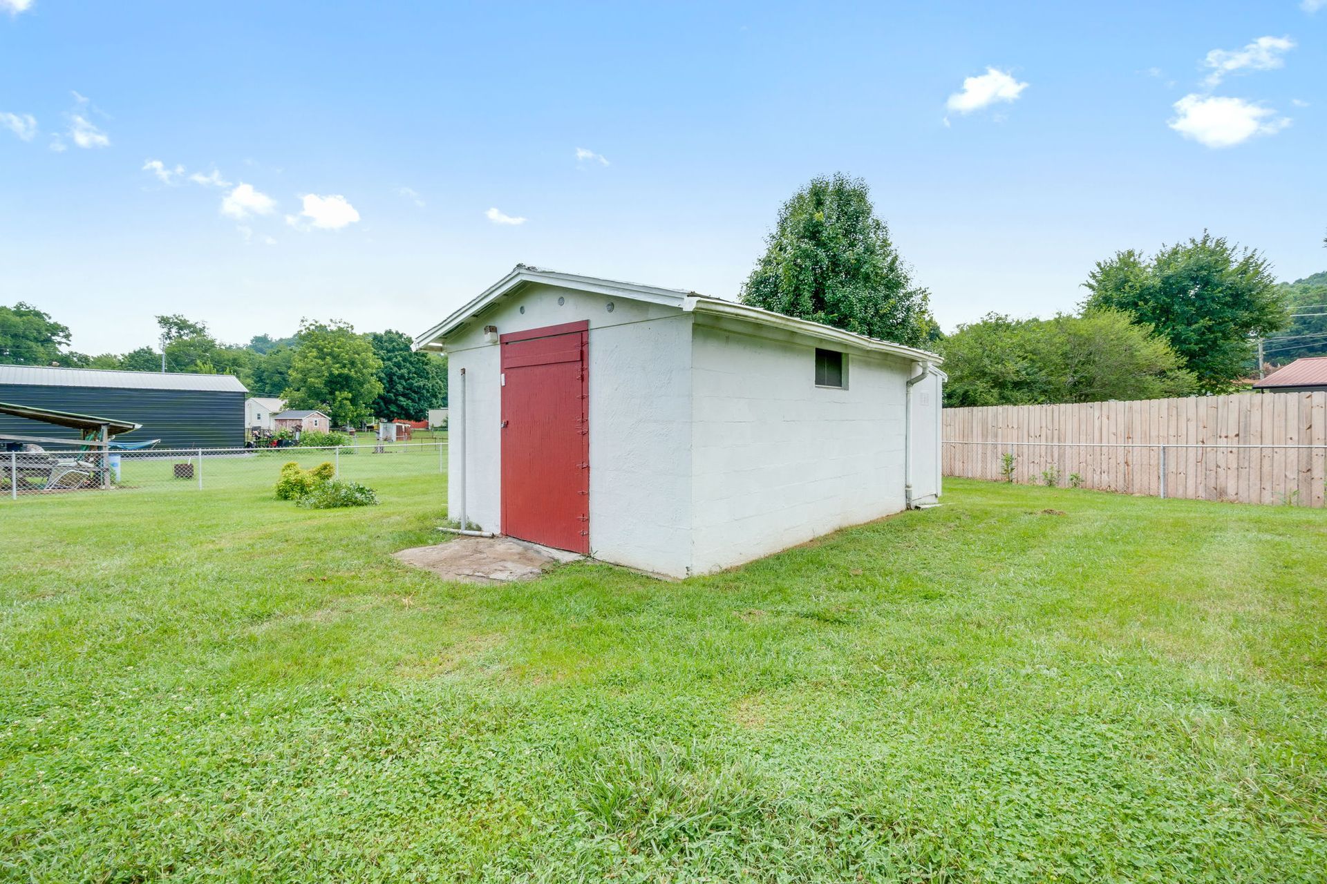 Small white shed with a red door in a grassy backyard under a blue sky
