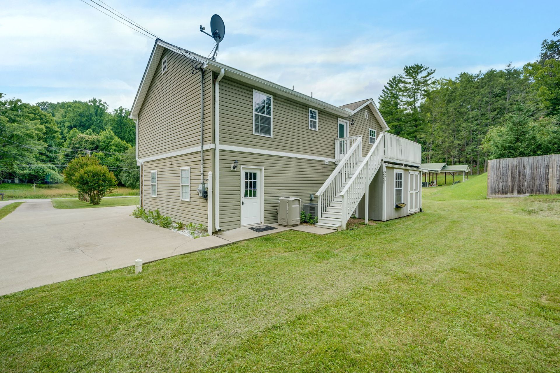 Two-story beige house with exterior stairs, white trim, and a grassy yard beside a driveway.
