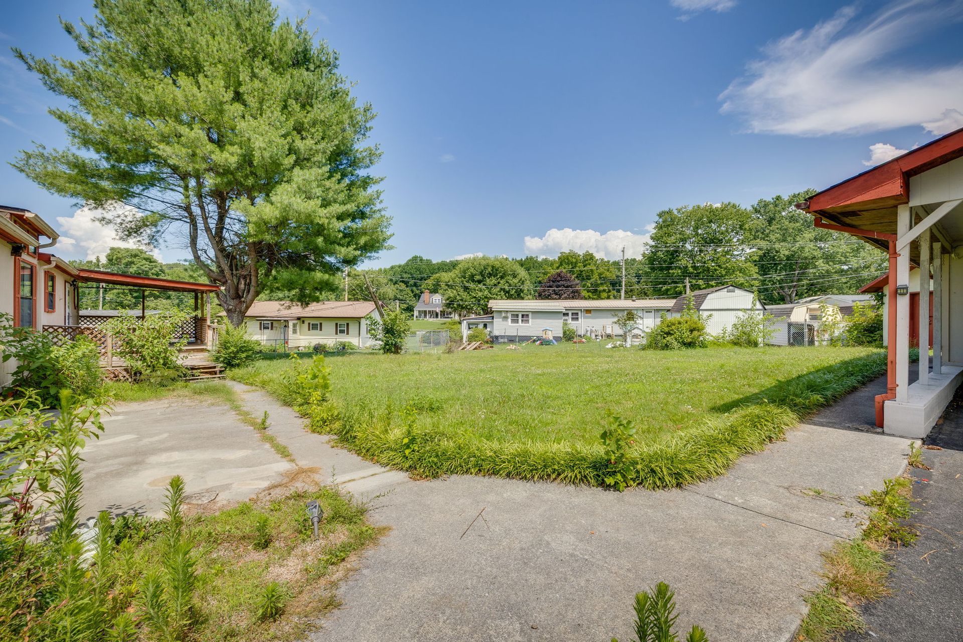 Grassy courtyard between low buildings with a large tree and paved path under a blue sky