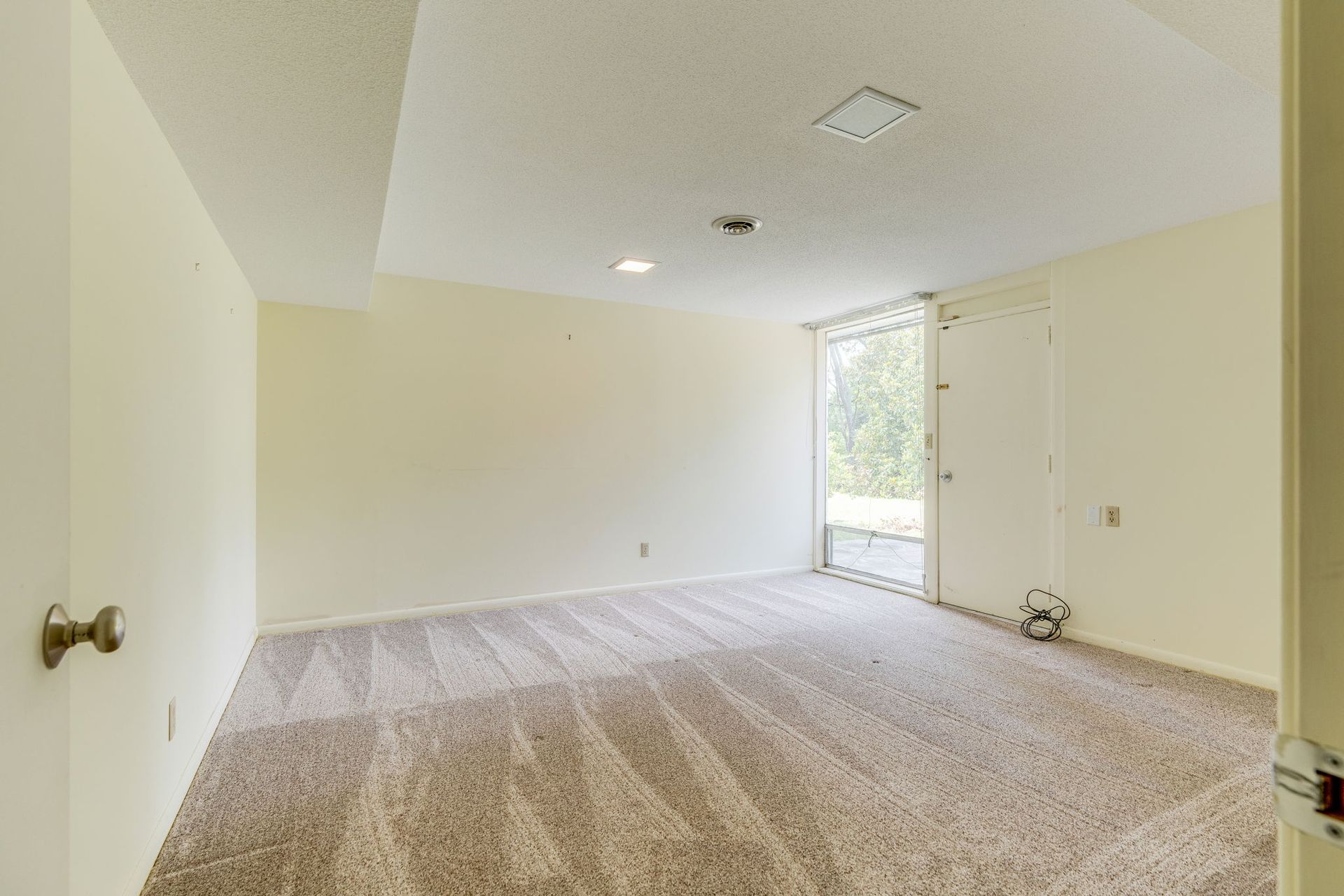 Empty beige carpeted room with white walls and a sliding glass door to a balcony.