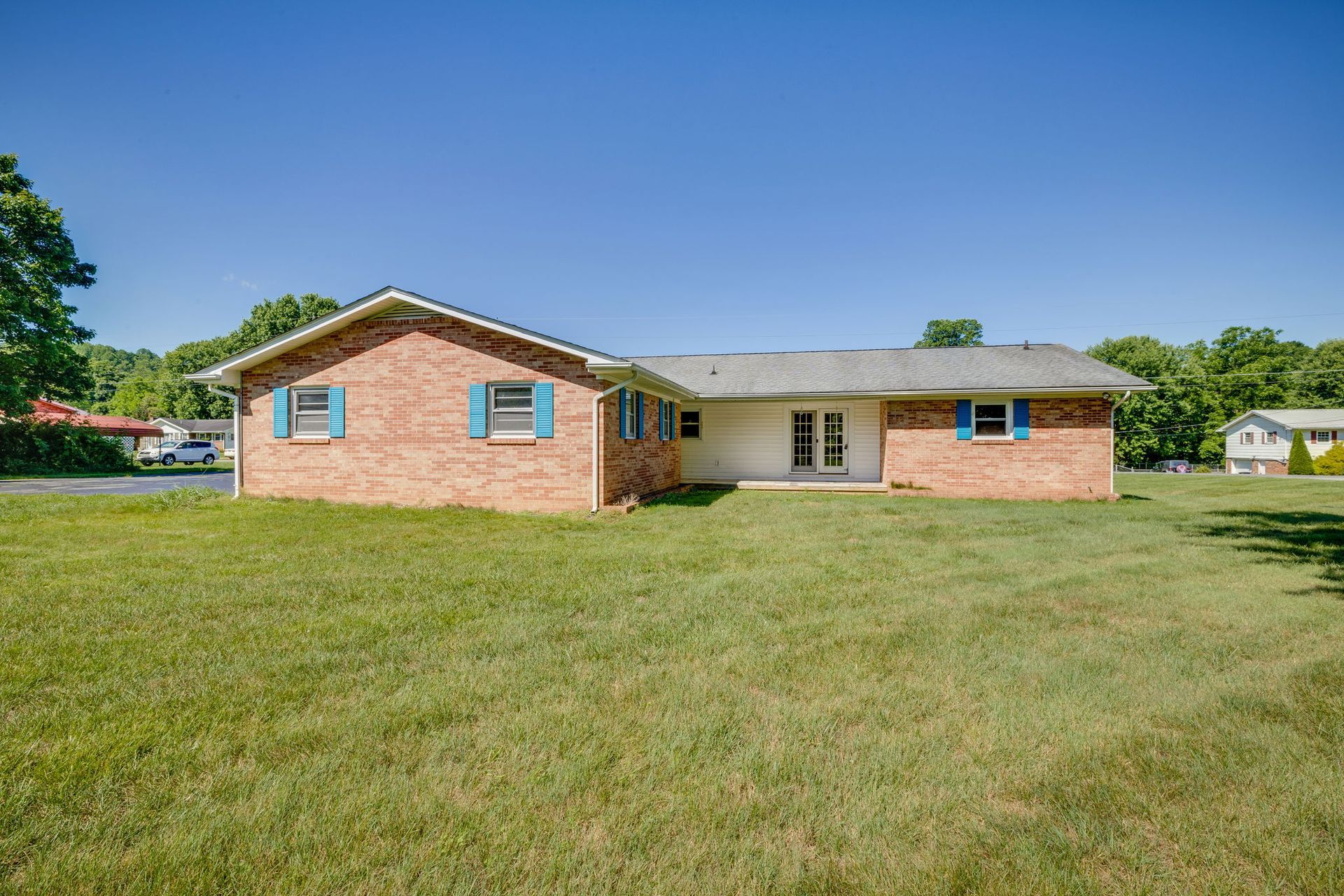 Single-story brick house with a wide grassy yard under a clear blue sky