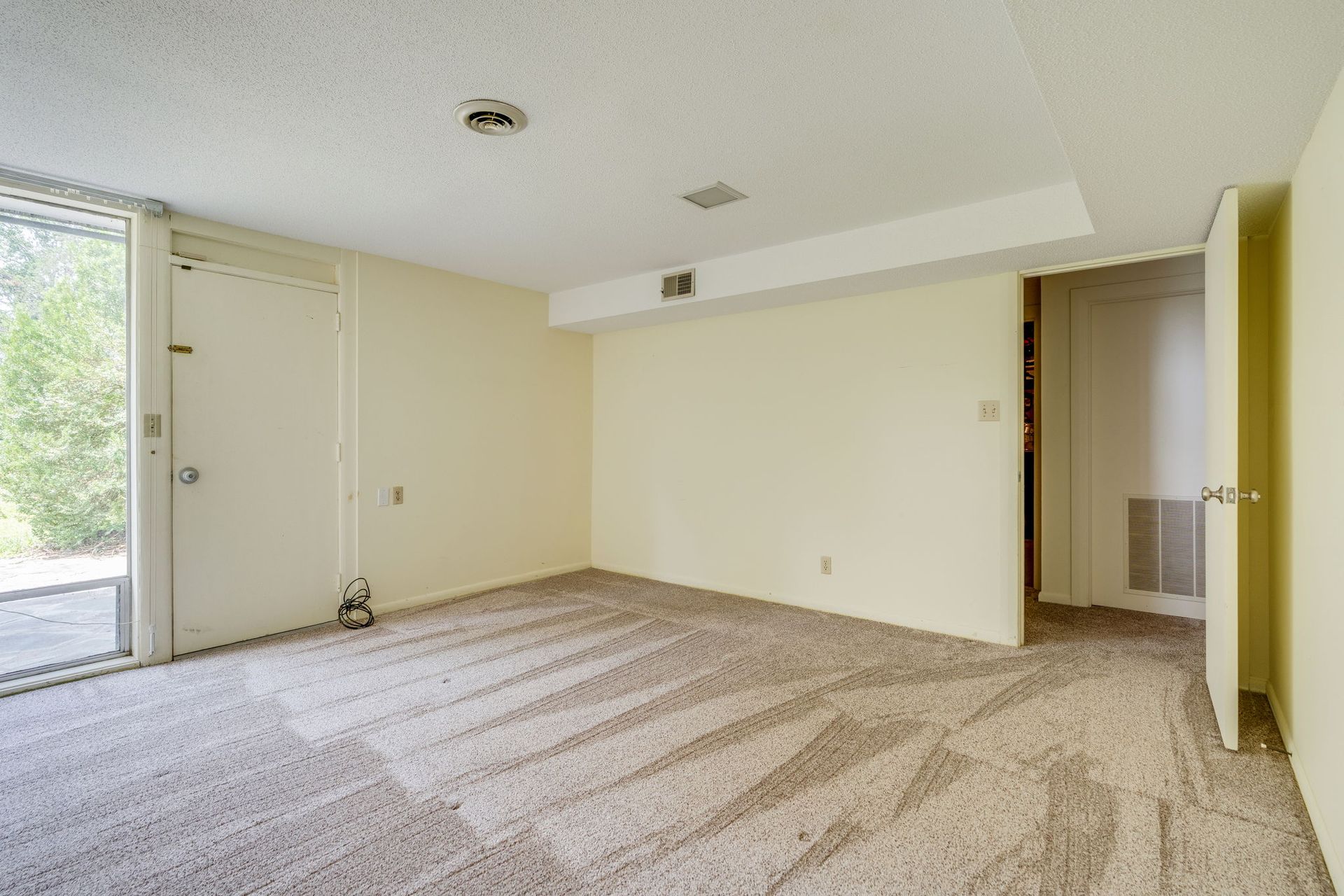 Empty beige carpeted living room with white walls, sliding glass door, and open doorway.