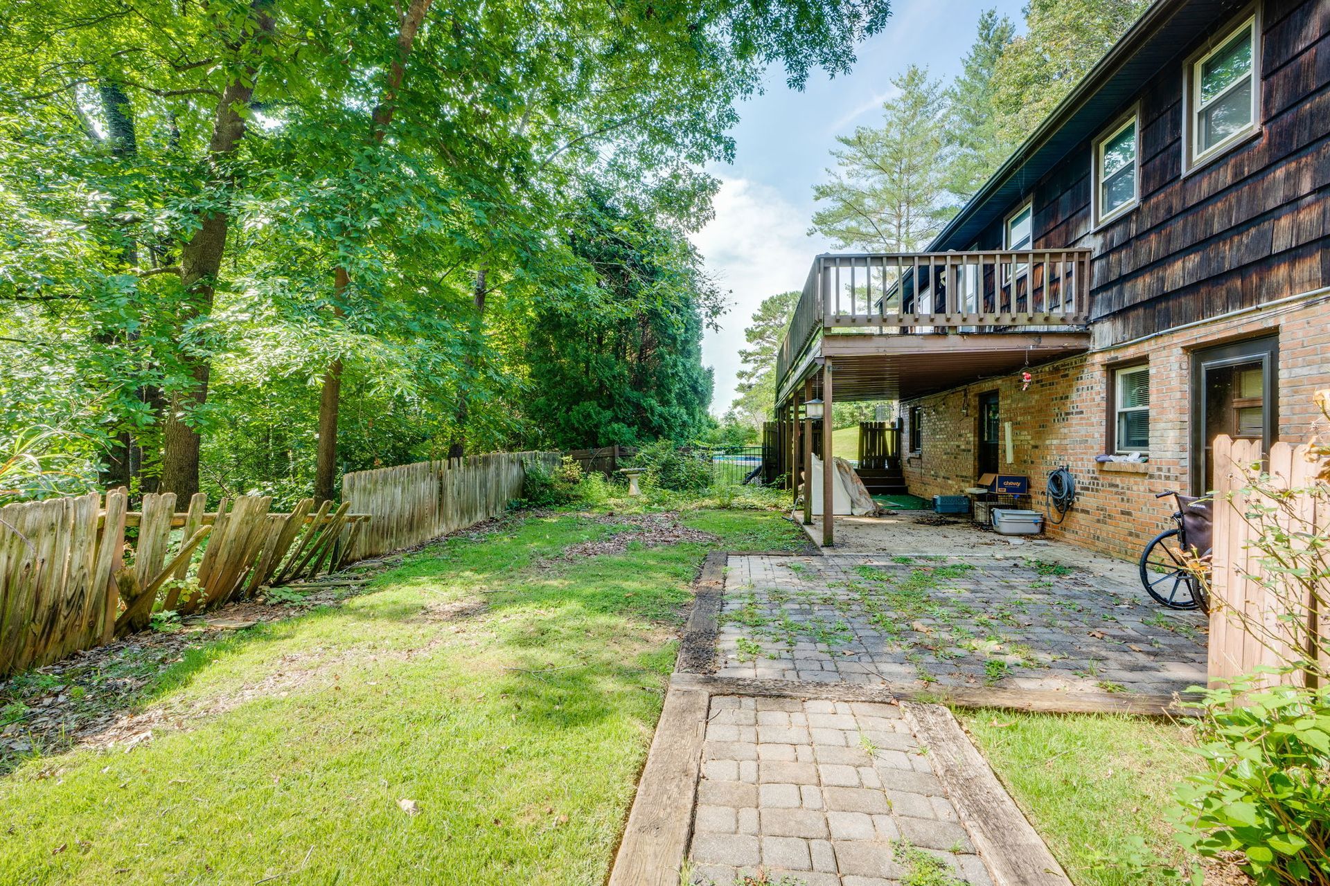 Backyard patio beside a house, with brick path, grass lawn, trees, and a fenced yard.