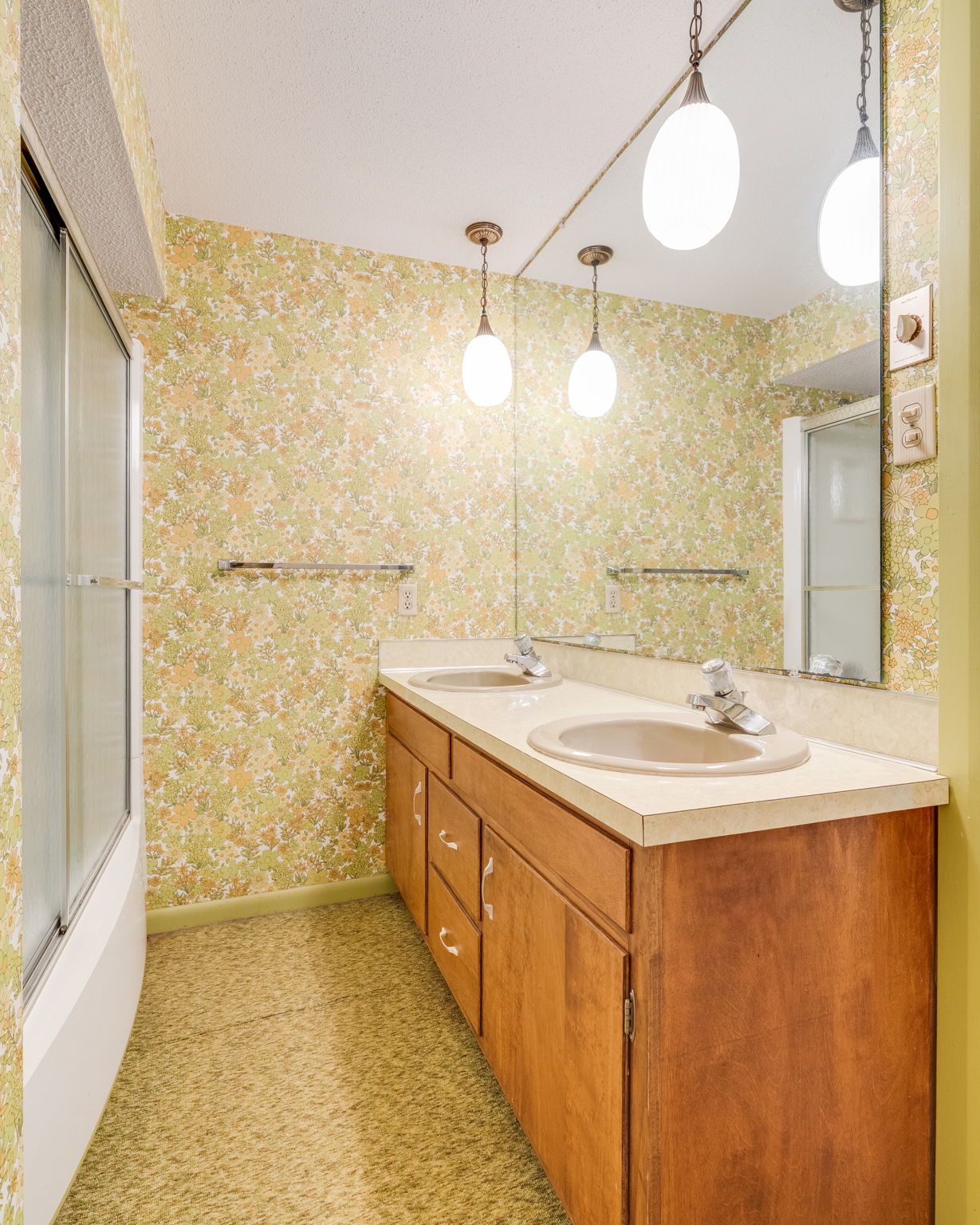 Small bathroom with floral wallpaper, double-sink vanity, large mirror, and pendant lights