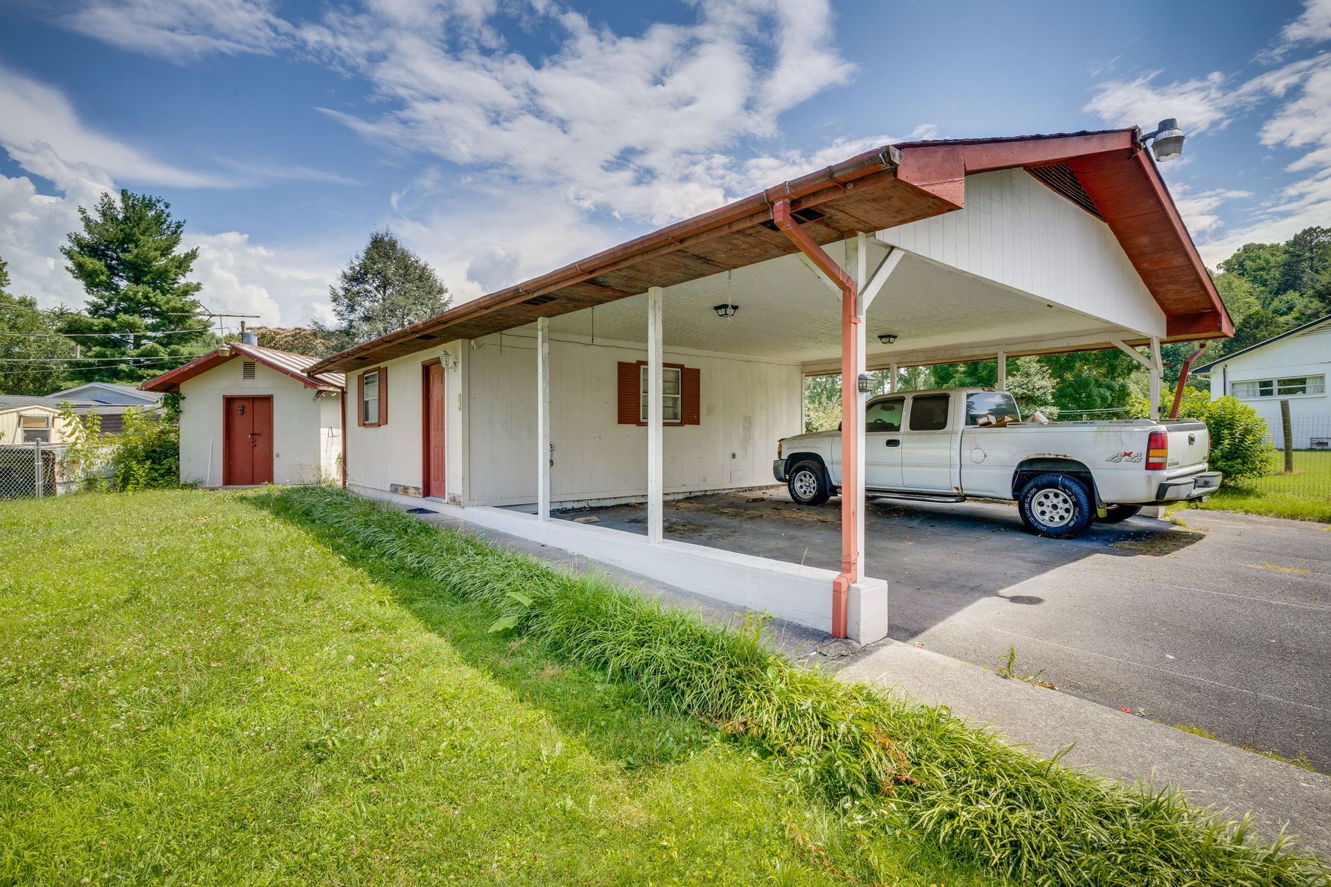 Single-story house with a covered carport, white walls, red roof, and a parked pickup truck.