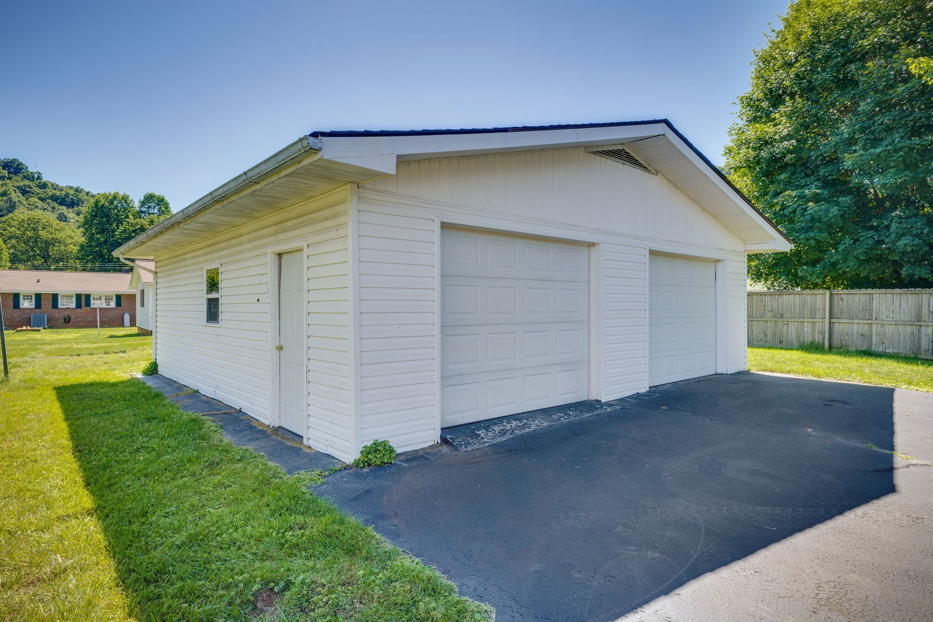 White detached two-car garage with a paved driveway and green lawn in bright sunlight
