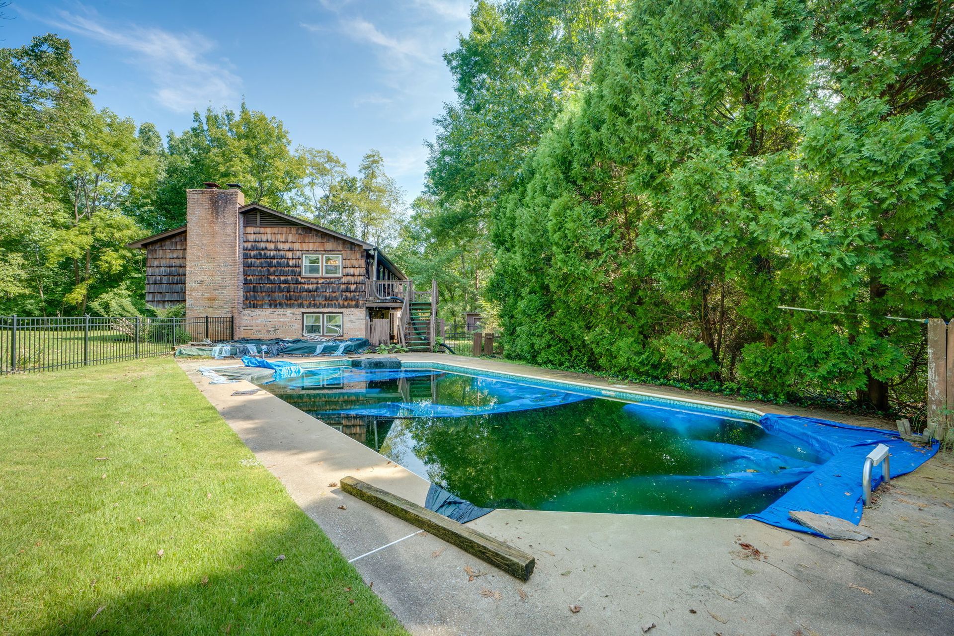 Backyard with a covered pool, green lawn, and brick house surrounded by trees