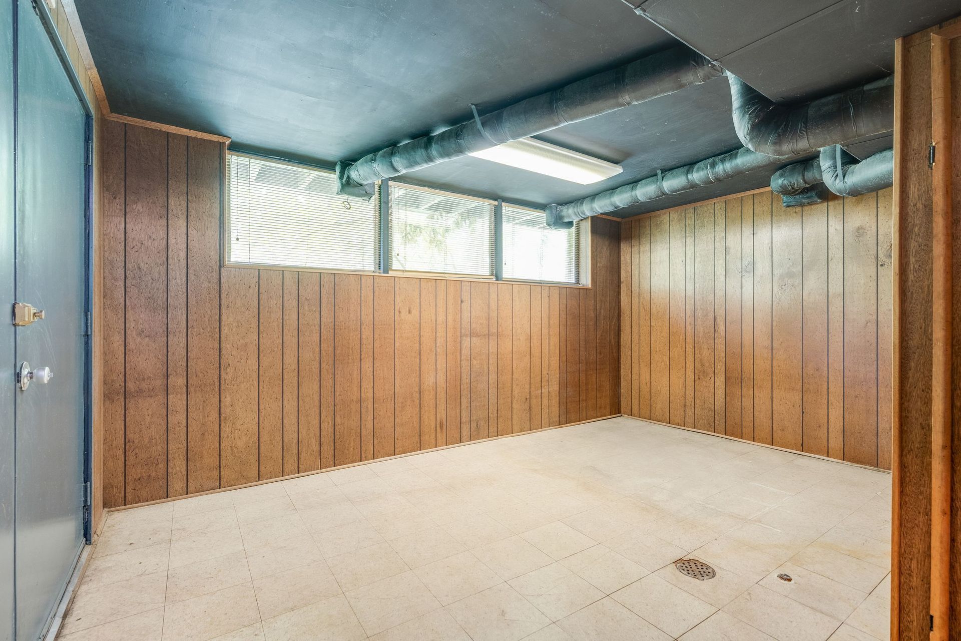Empty unfinished basement room with wood-paneled walls, low ceiling, and exposed ducts