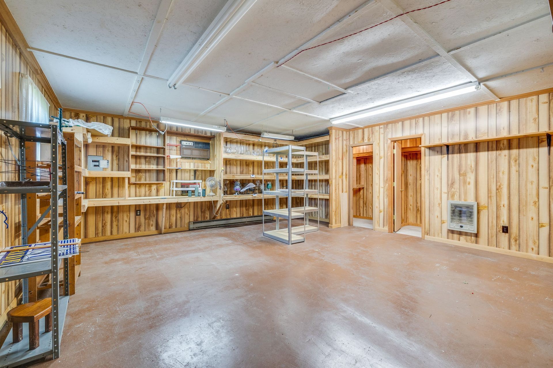 Empty basement workshop with wood-paneled walls, shelving, and a polished concrete floor