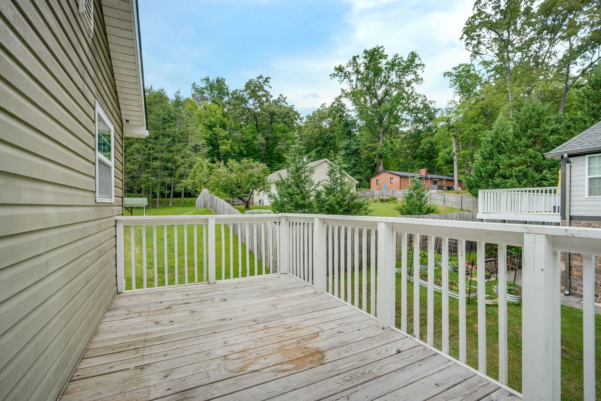 White wooden deck with railing beside a beige house, overlooking a green backyard and trees