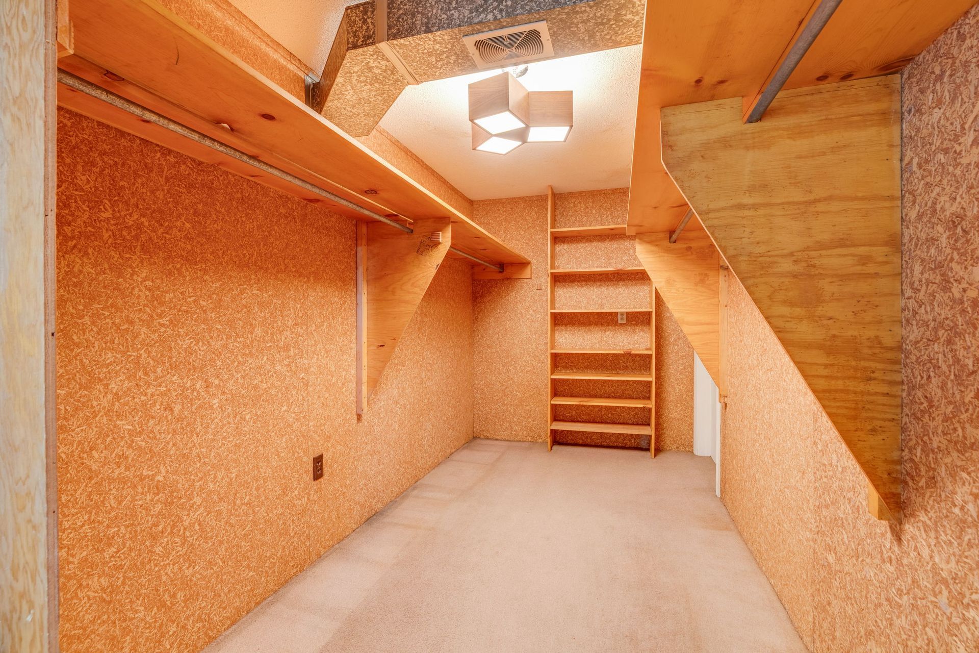 Small unfinished room with wood-paneled walls, carpeted floor, and staircase under a ceiling light.