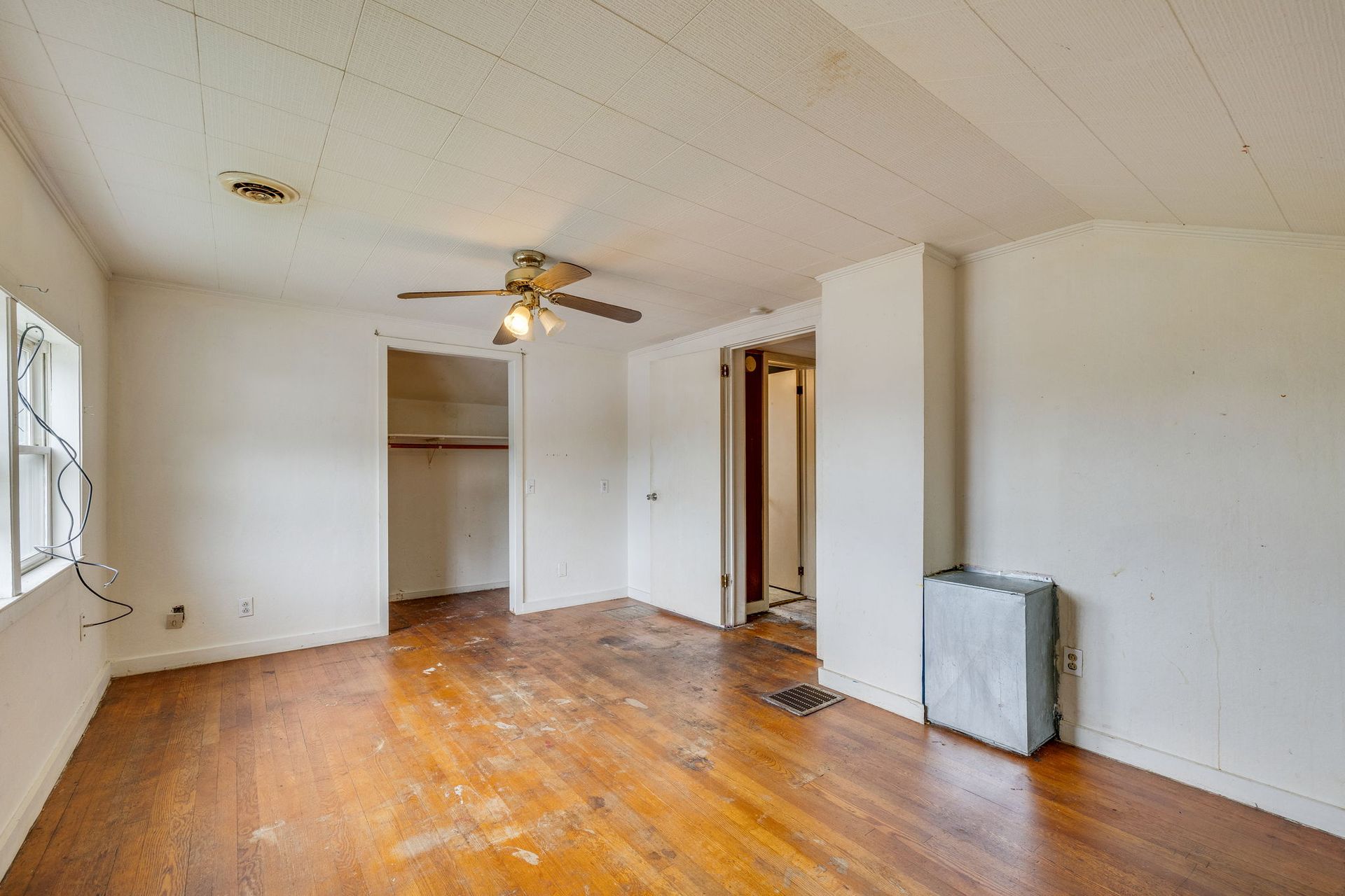 Empty white room with hardwood floors, ceiling fan, window, and open closet doorway