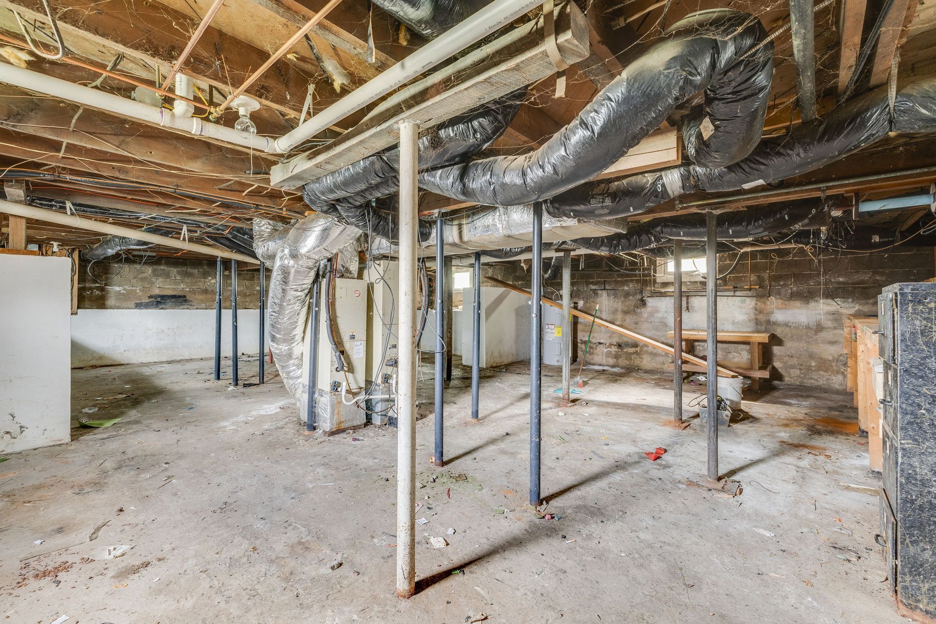 Unfinished basement with exposed beams, ducts, and metal framing on a concrete floor.