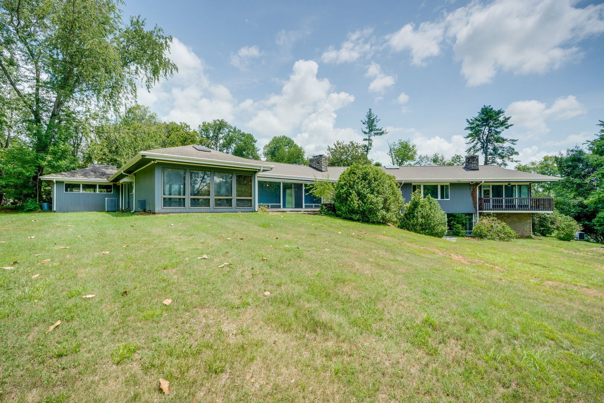 Single-story blue house with a large grassy front yard and trees under a partly cloudy sky