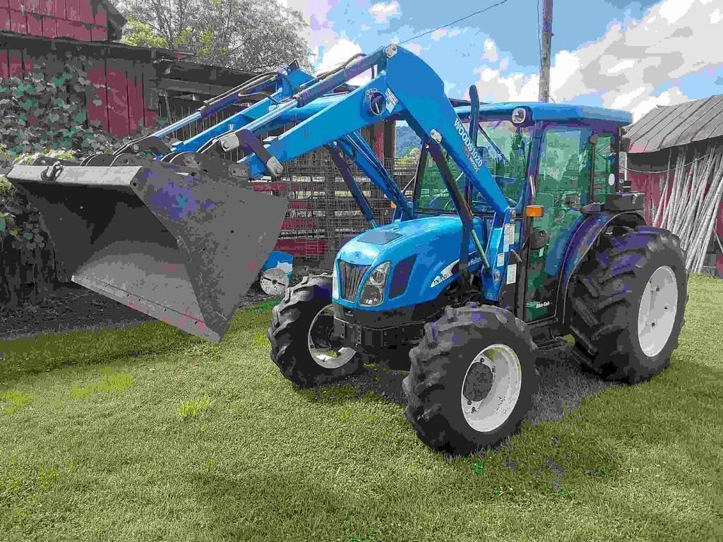 Blue tractor with front loader and bucket parked on grass in a yard