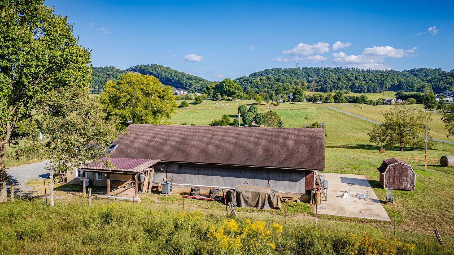 Rural barn with a brown roof in a green hillside field under a clear blue sky