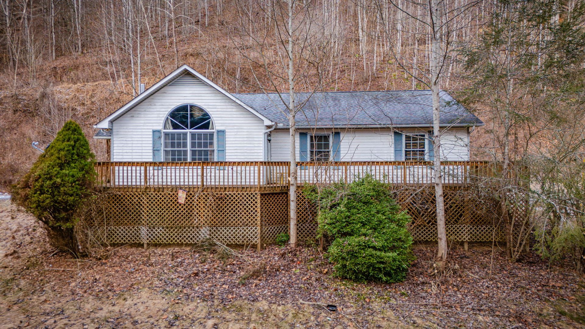 White house with wooden deck, surrounded by trees on a hillside.