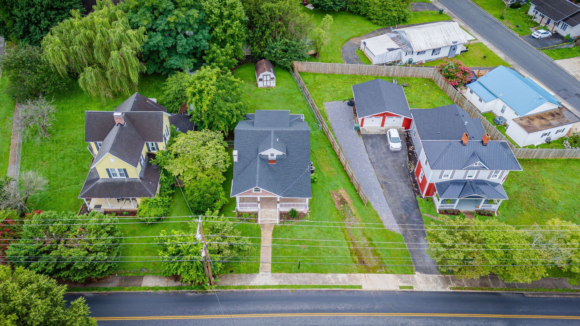 Aerial view of three suburban houses with lawns, driveways, and a road in front.
