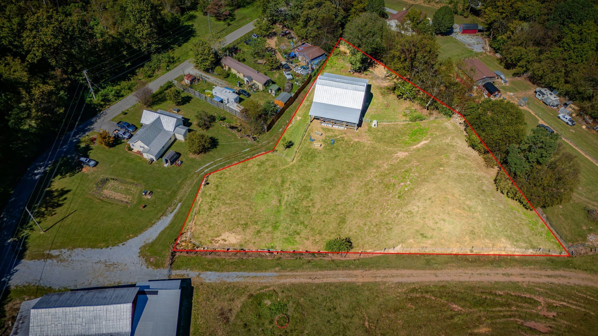 Aerial view of a grassy lot outlined in orange beside houses and a white building, near a road and trees