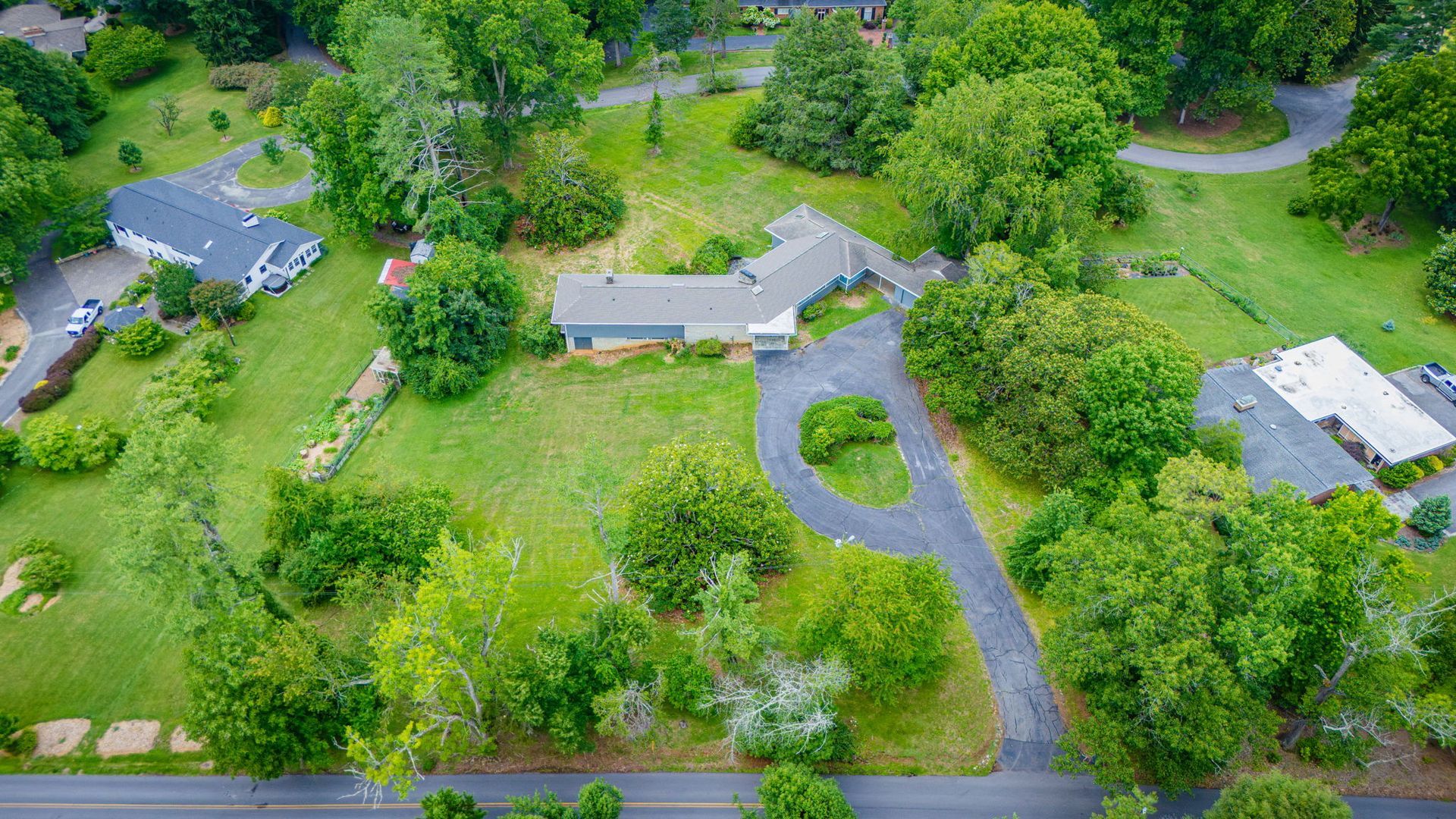 Aerial view of a rural property with several houses, winding driveway, and lush green trees.