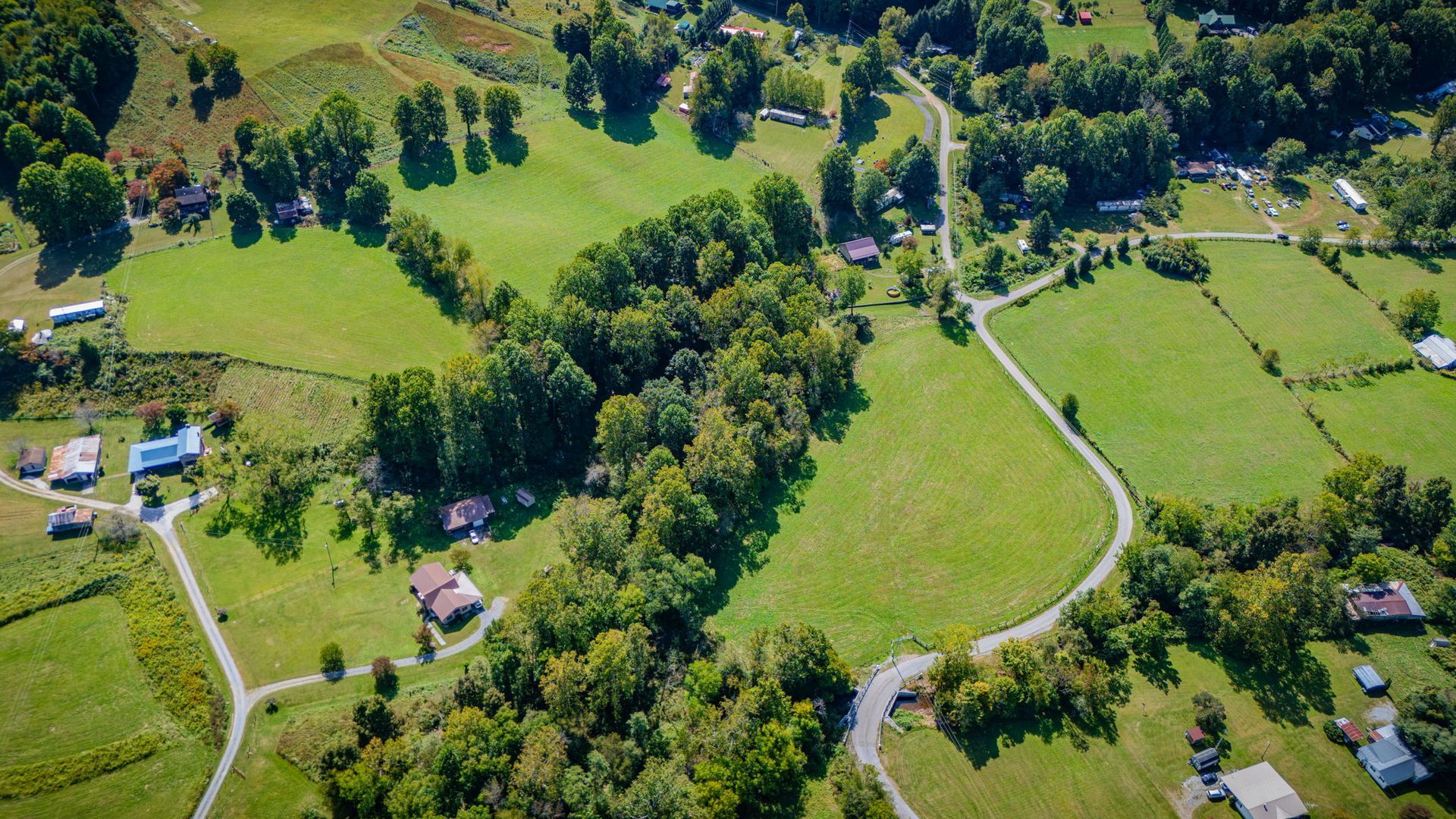 Aerial view of a green rural landscape with fields, trees, winding roads, and scattered houses.