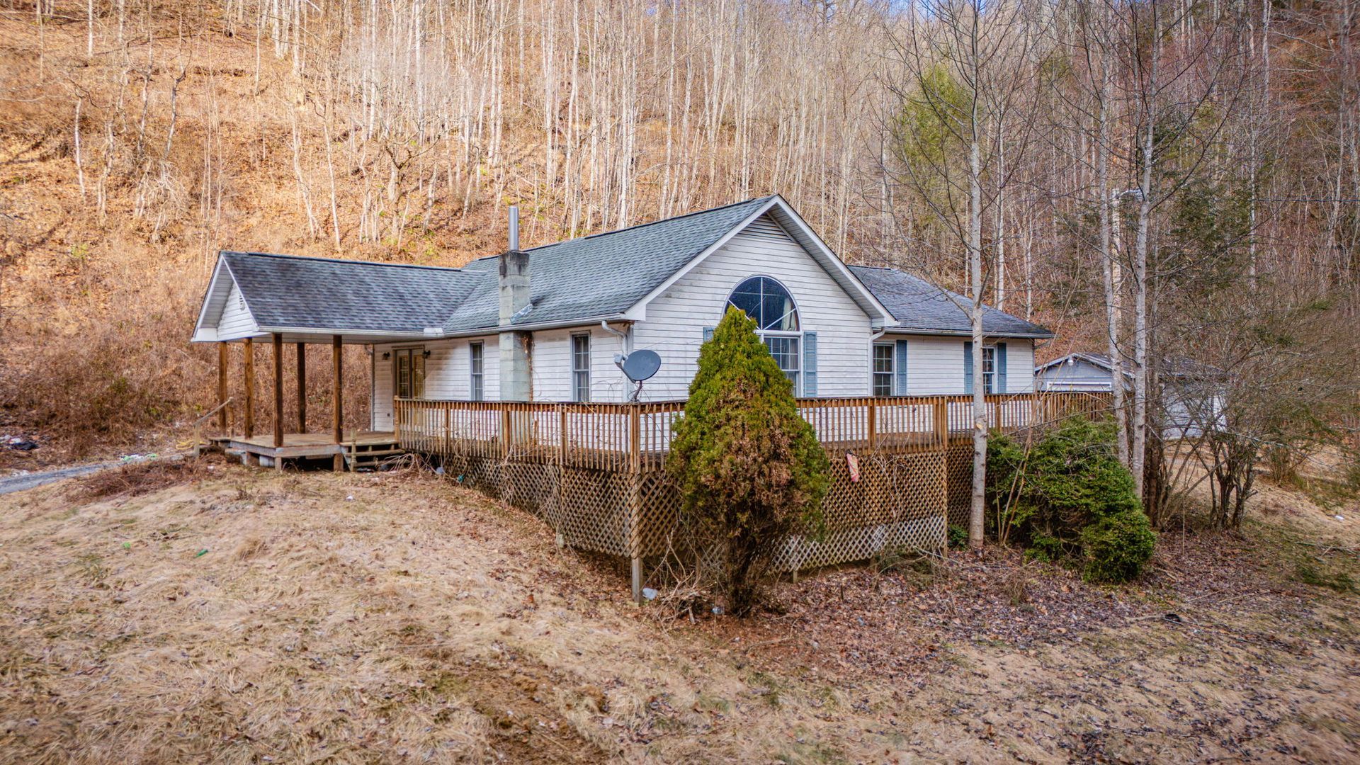 White house with deck and covered porch nestled among bare trees on a hillside.