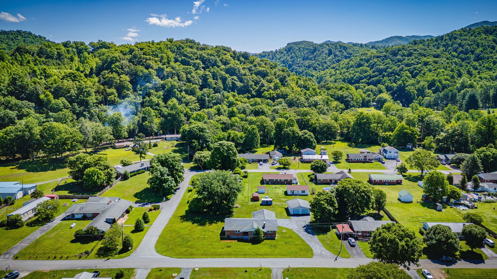 Aerial view of a small neighborhood with houses, roads, and lush green hills in the background